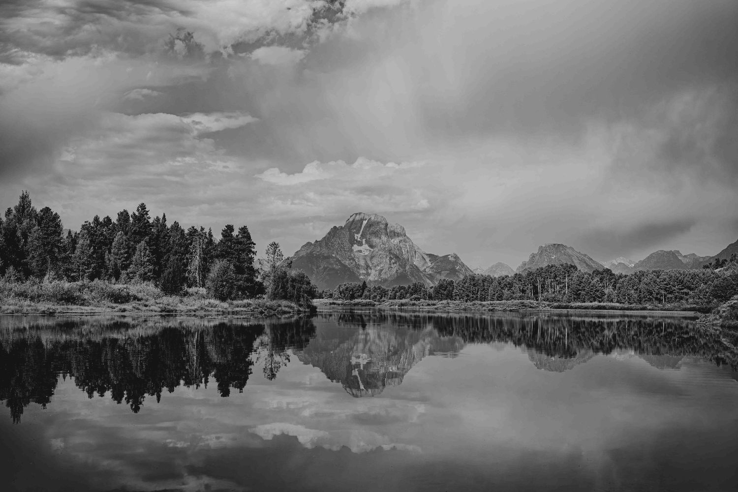 Dramatic black and white panoramic view of the Grand Teton mountains reflecting in the calm waters of Snake River.