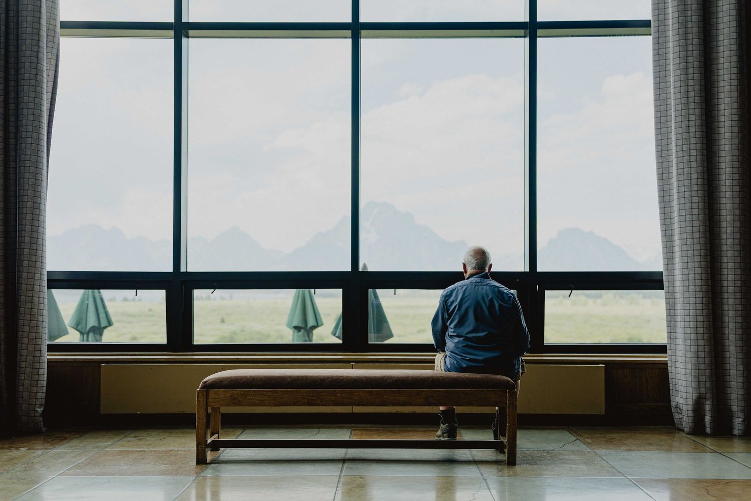 Solitary figure seated on bench overlooking large windows with ocean view.