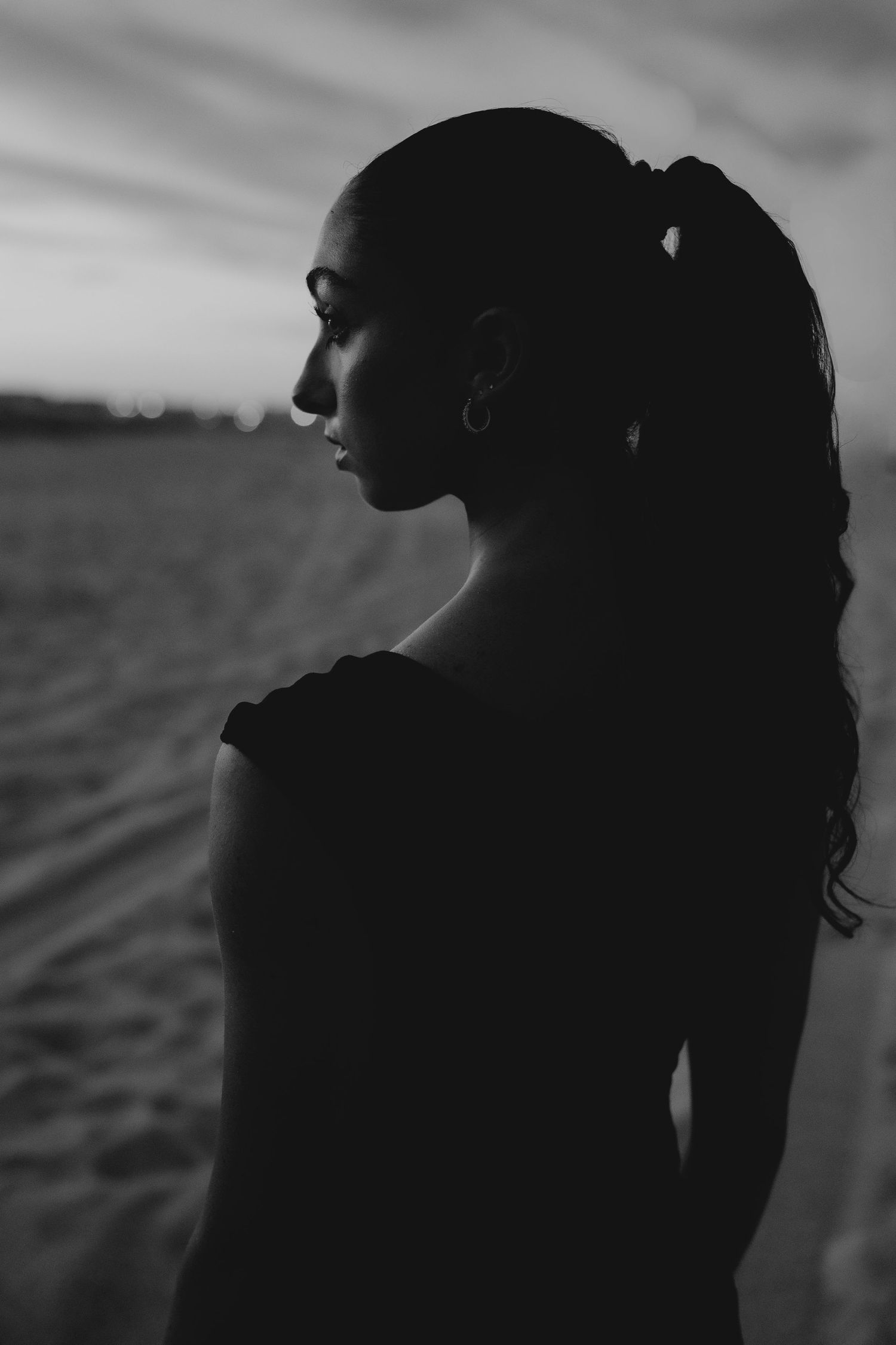 Black and white silhouette portrait of young woman with ponytail at beach during sunset.