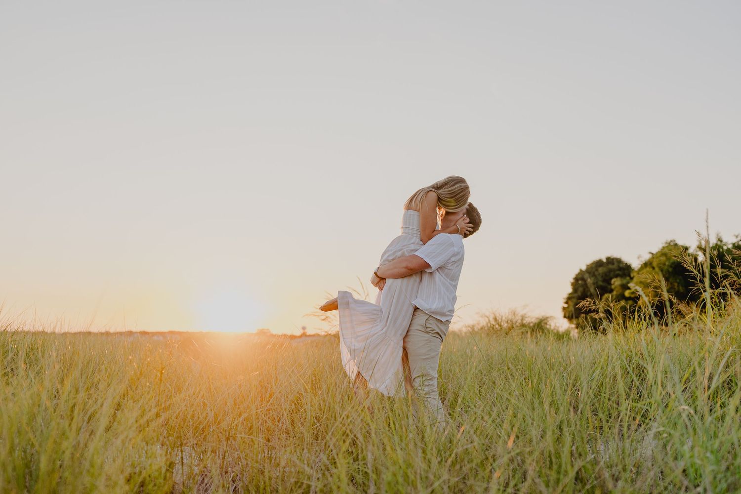 Couple embracing in golden sunset light in a grassy field.