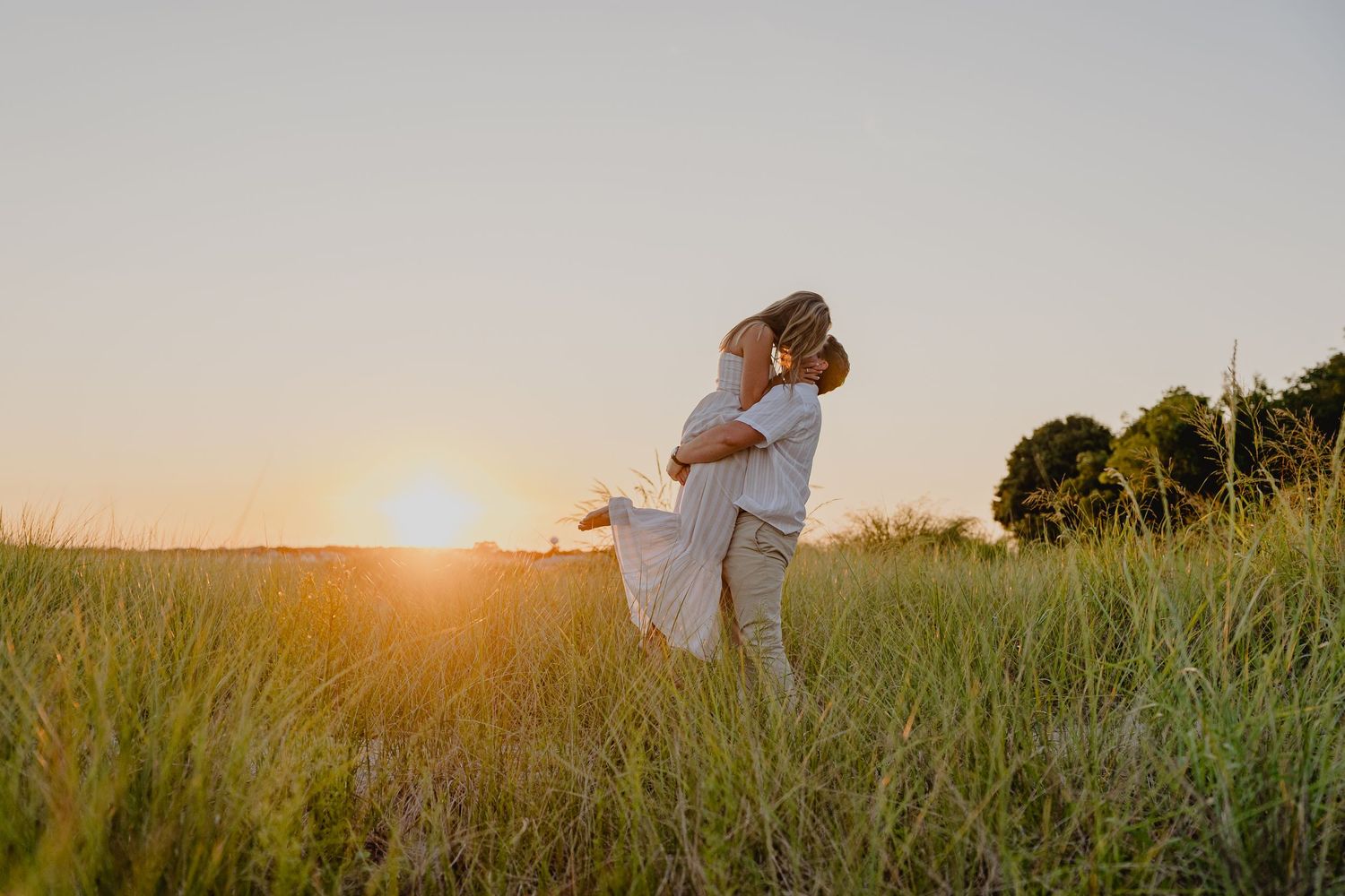 Couple embracing in golden sunset light in a lush green field, romantic outdoor engagement photo.