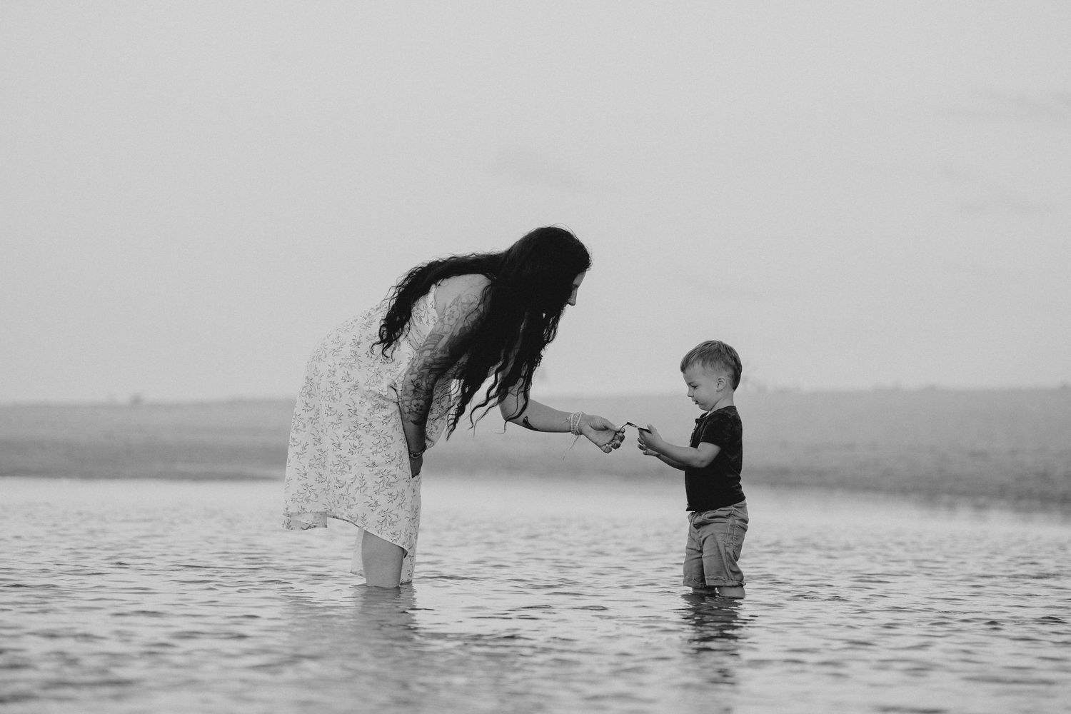 A couple embraces while standing in shallow water at sunset creating a romantic silhouette.