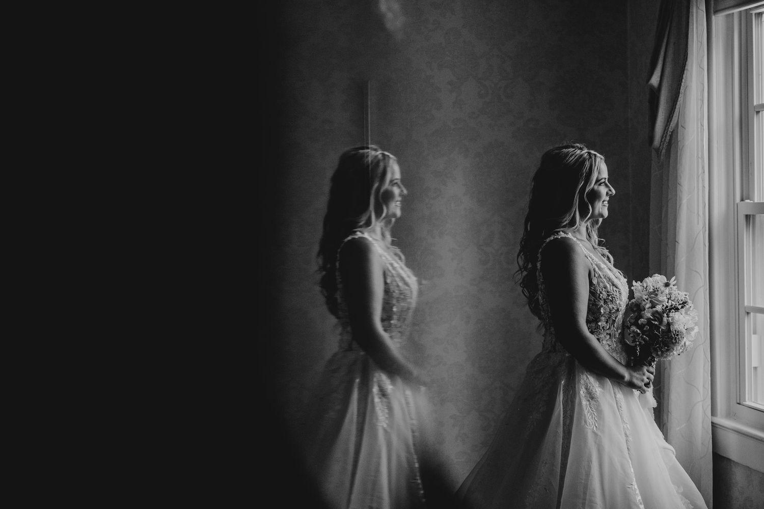 Artistic black and white silhouette of bride in wedding dress by window.