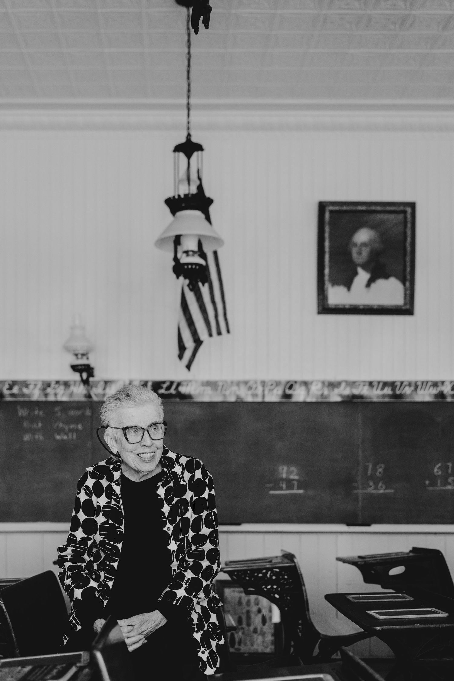 A person wearing a star-patterned sweater sits in a classroom with chalkboards and framed artwork on the walls.