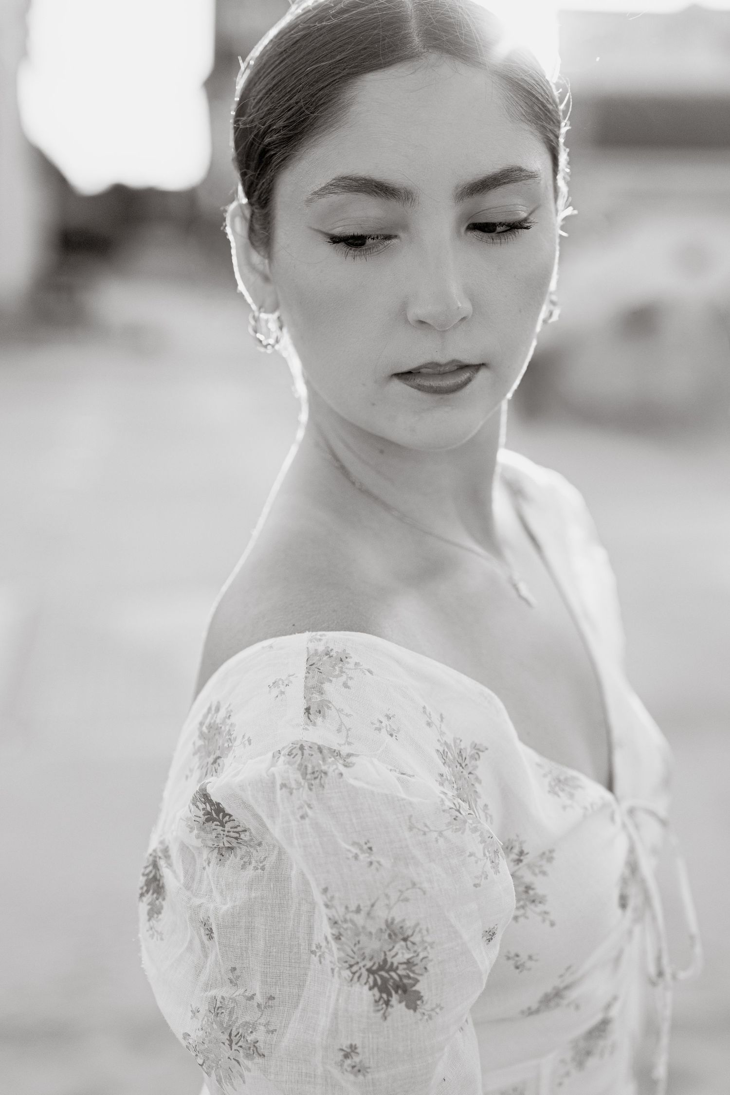 Black and white portrait of a young woman in an off-shoulder floral dress, looking down gracefully.