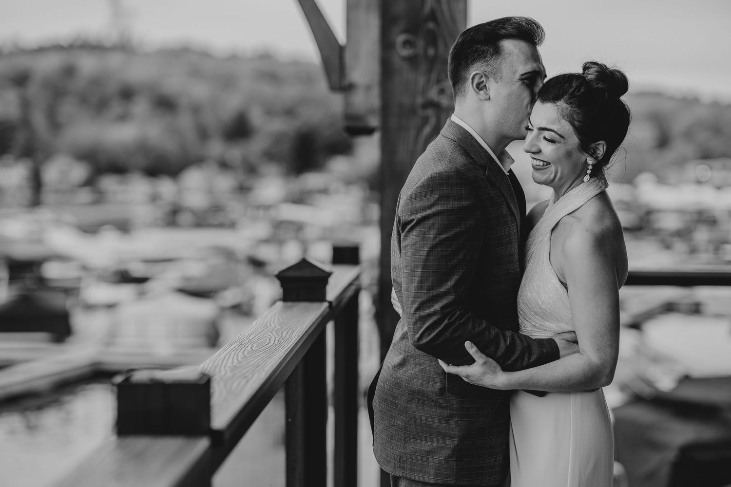 A couple in wedding attire shares candid moments on a deck with marina views.