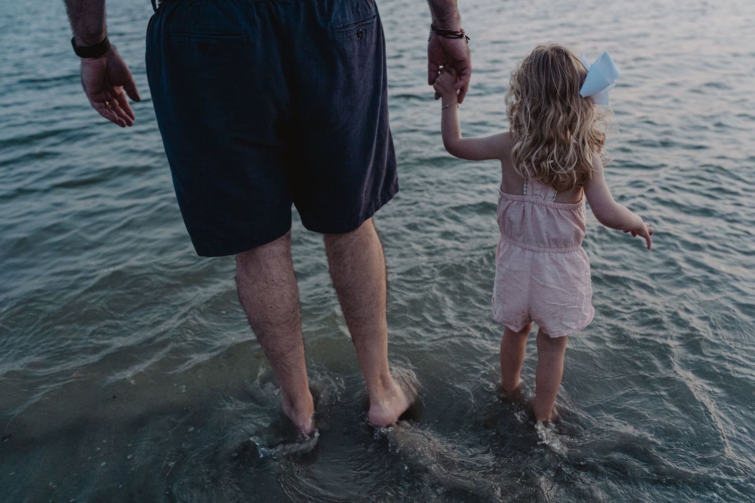 Feet and legs splashing in shallow ocean water during sunset.