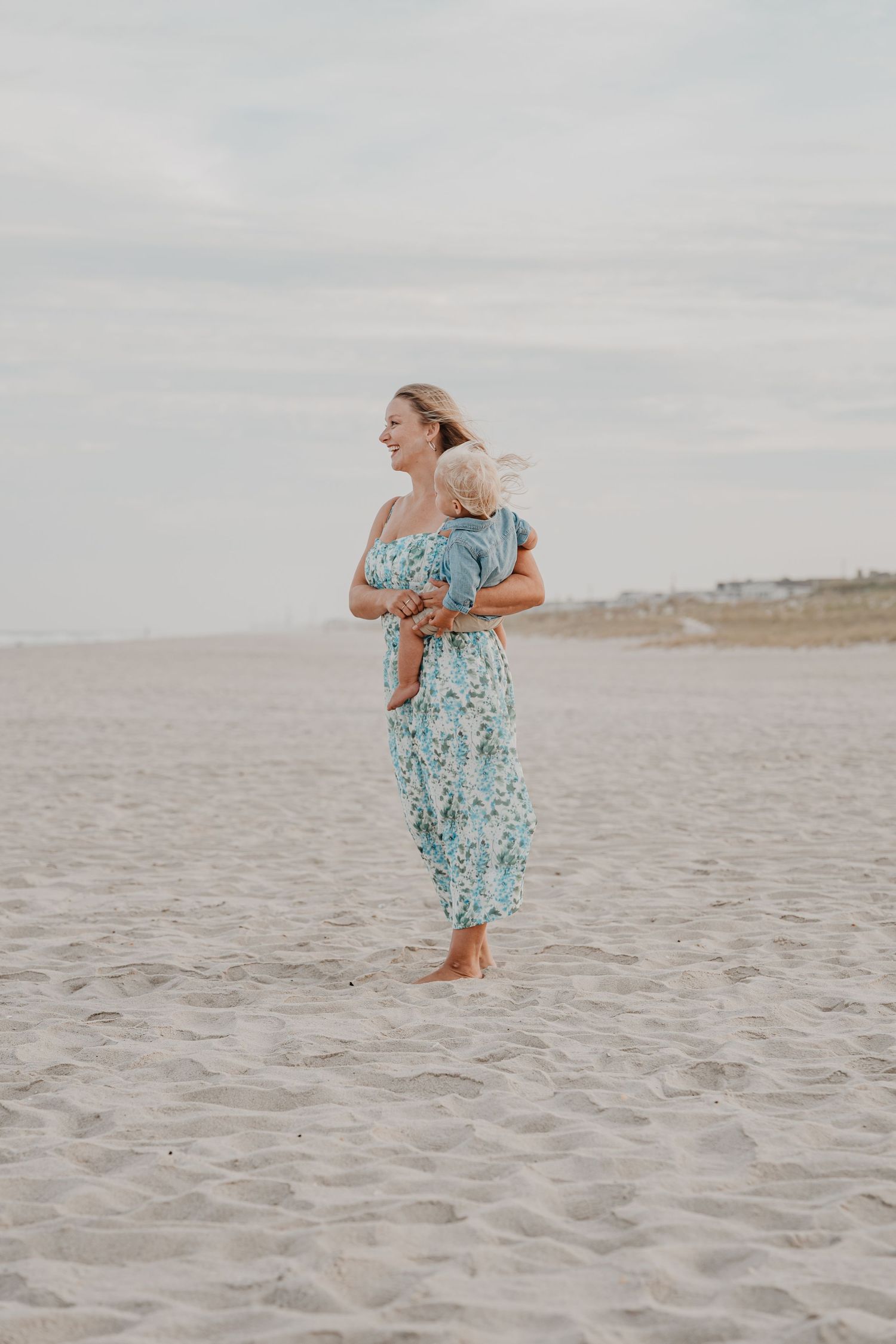 Woman in floral dress playing and spinning on beach at sunset.