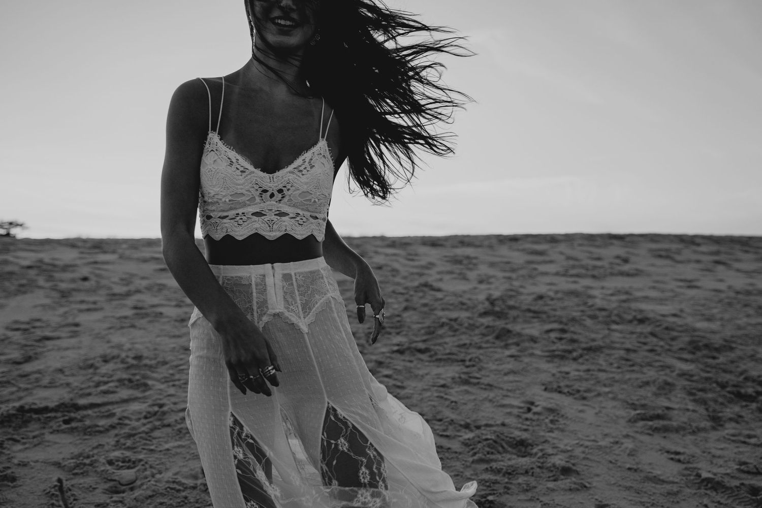 Black and white photo of a woman in a lace crop top and flowing skirt walking on a sandy beach. Sea Girt New Jersey