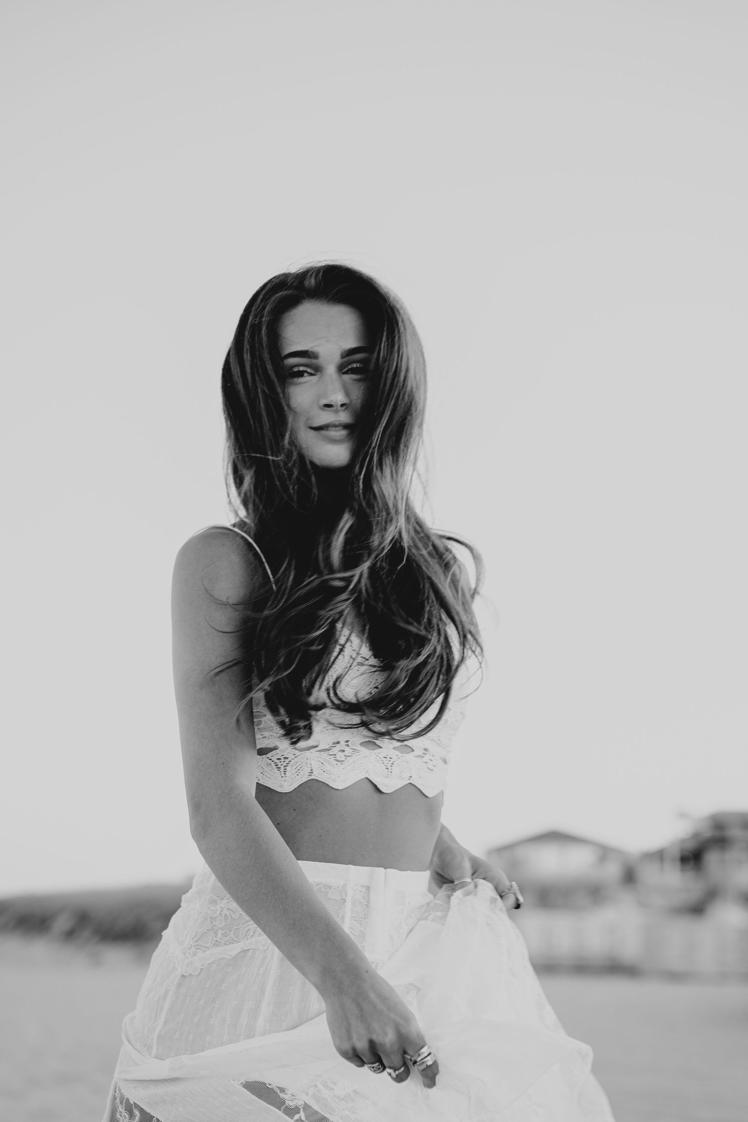 Black and white portrait of a young woman with long hair wearing a white crop top and skirt outdoors.
