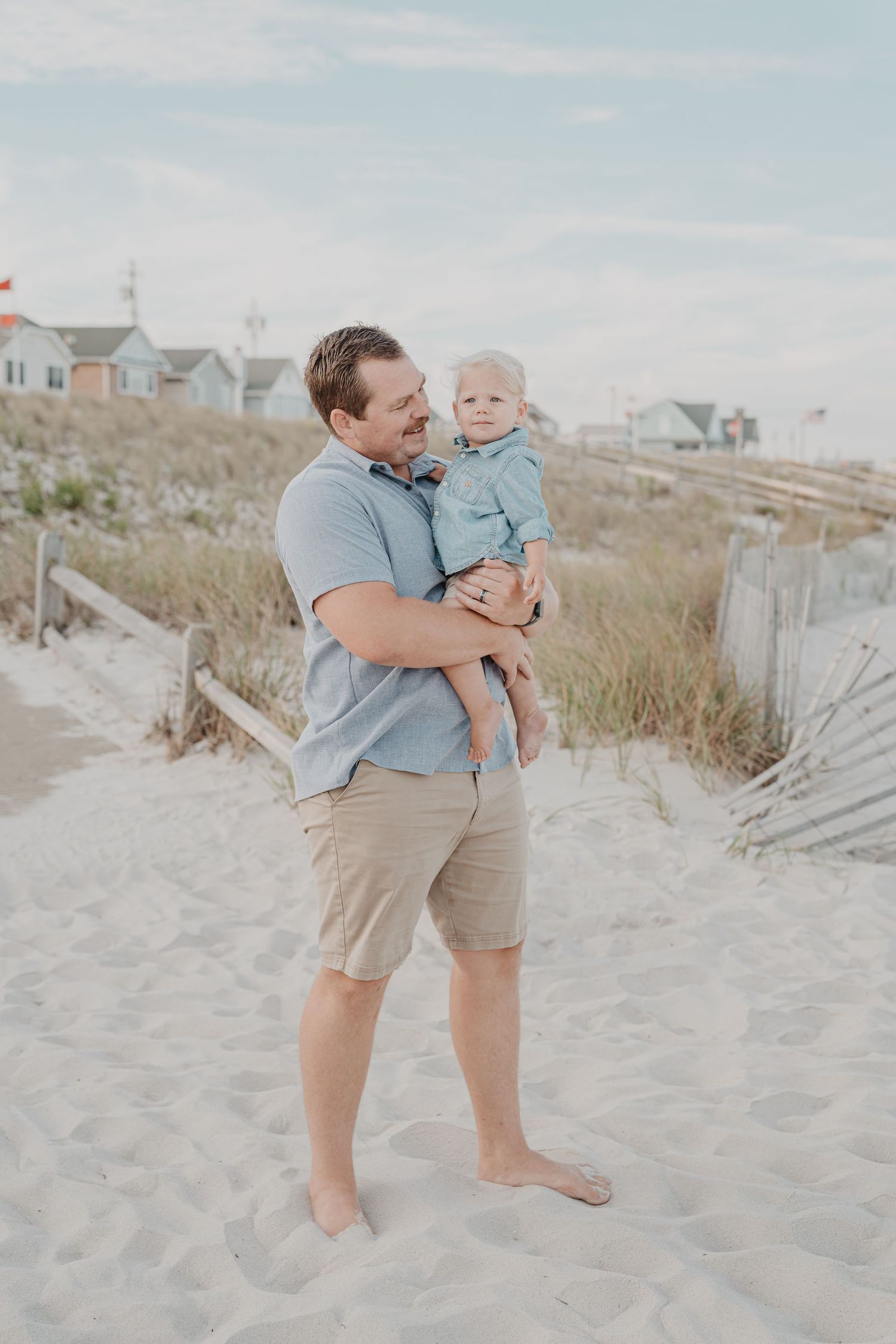 Parent and child playing together on sandy beach path near coastal homes.
