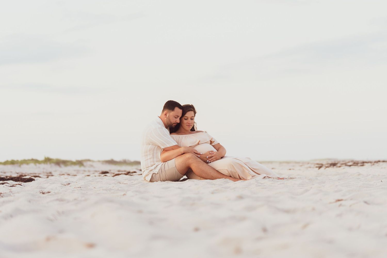 Romantic couple sitting together on sandy beach at sunset.