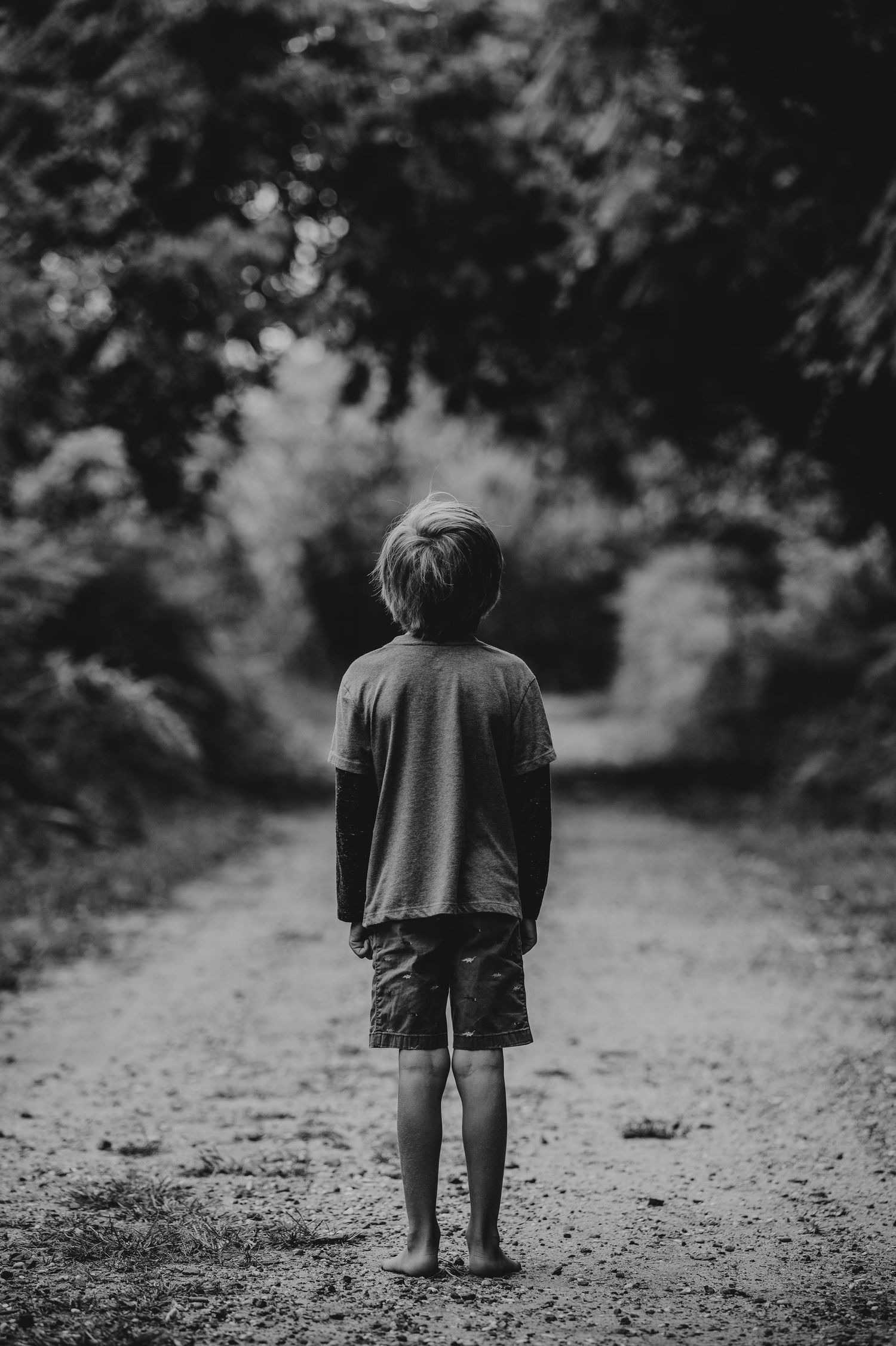 Black and white image of small child walking alone on forest path.