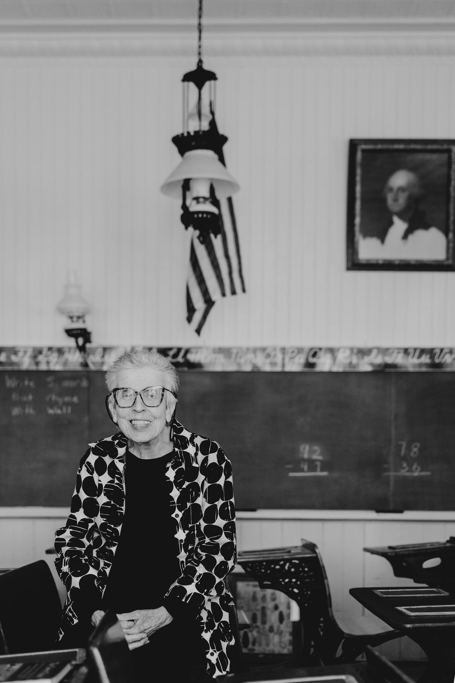 A black and white photograph shows someone wearing a star-patterned sweater seated at a desk in a classroom setting.