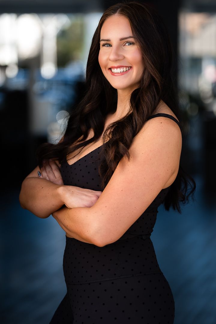 A person wearing a black sleeveless dress poses outdoors against a blurred urban background.