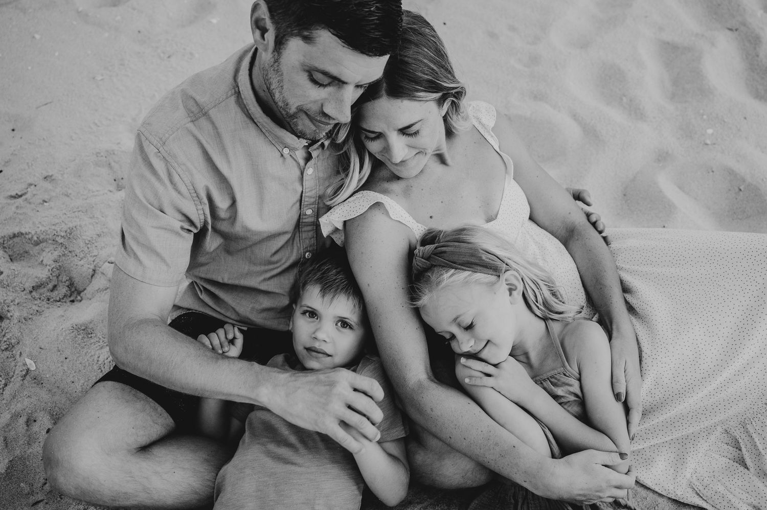 Intimate black and white family portrait on sandy beach.