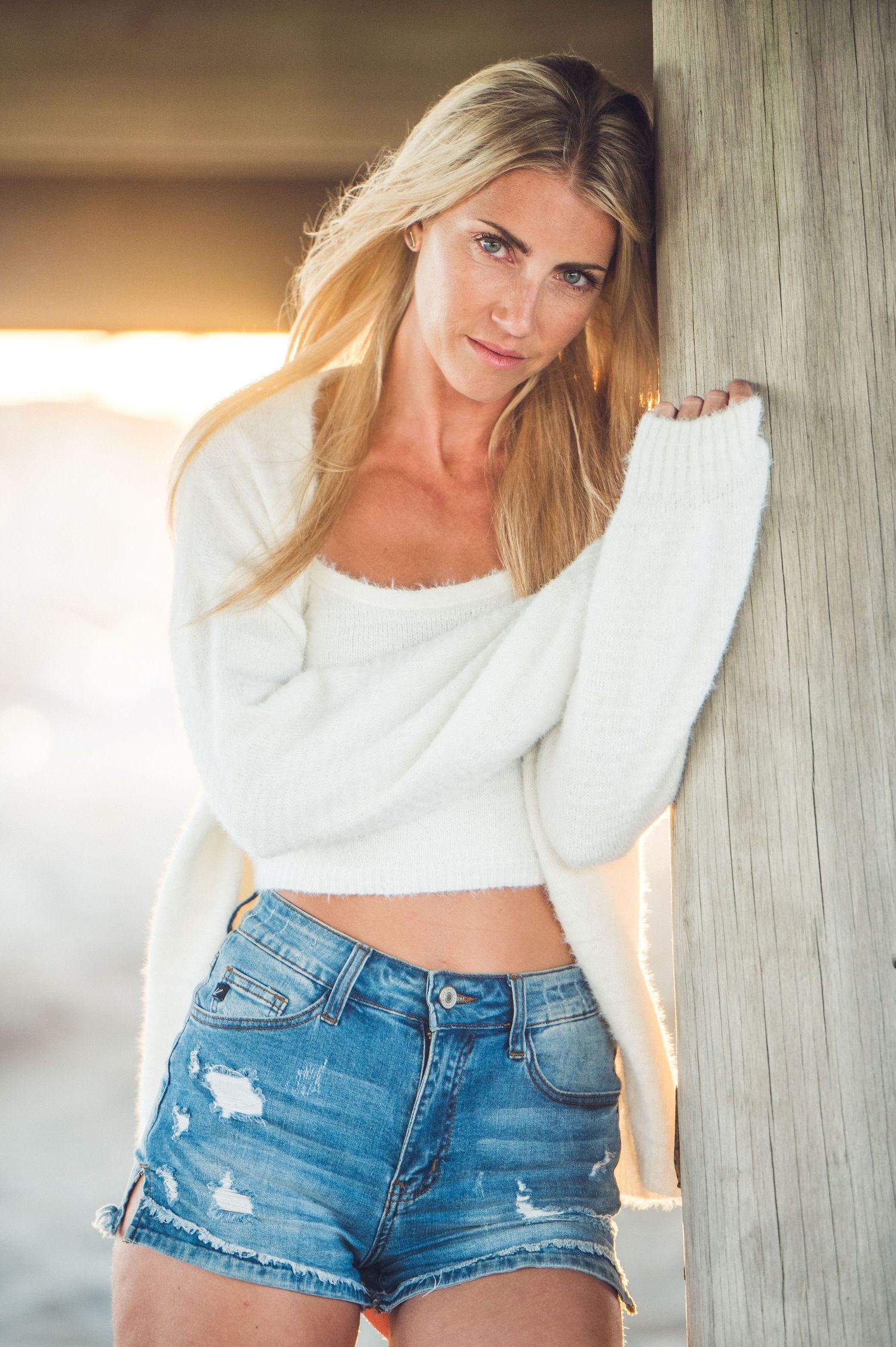 Fashion portrait of someone wearing a white cropped sweater and distressed denim shorts in warm sunlight.