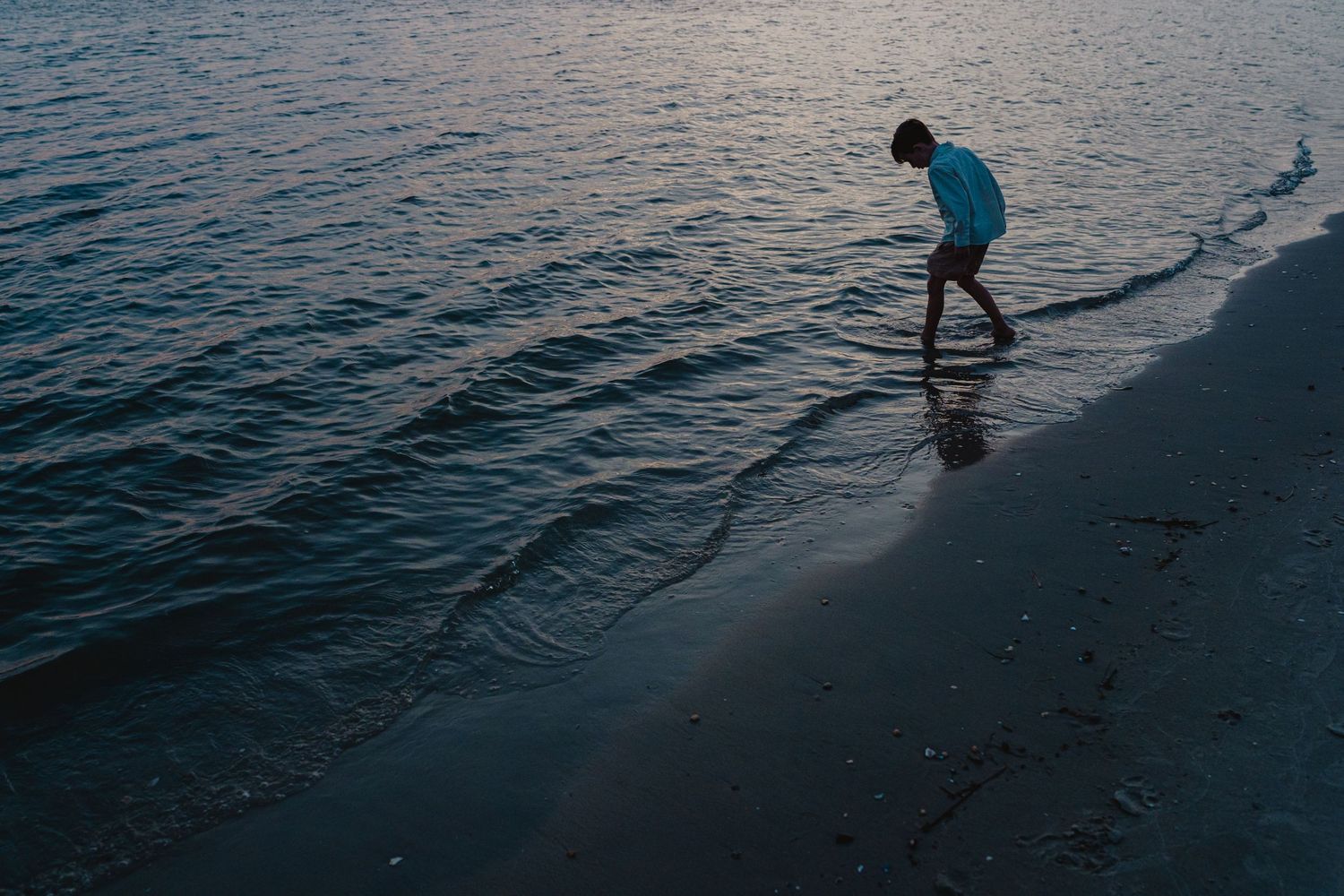Silhouettes of people walking along a beach at dusk with calm waters.