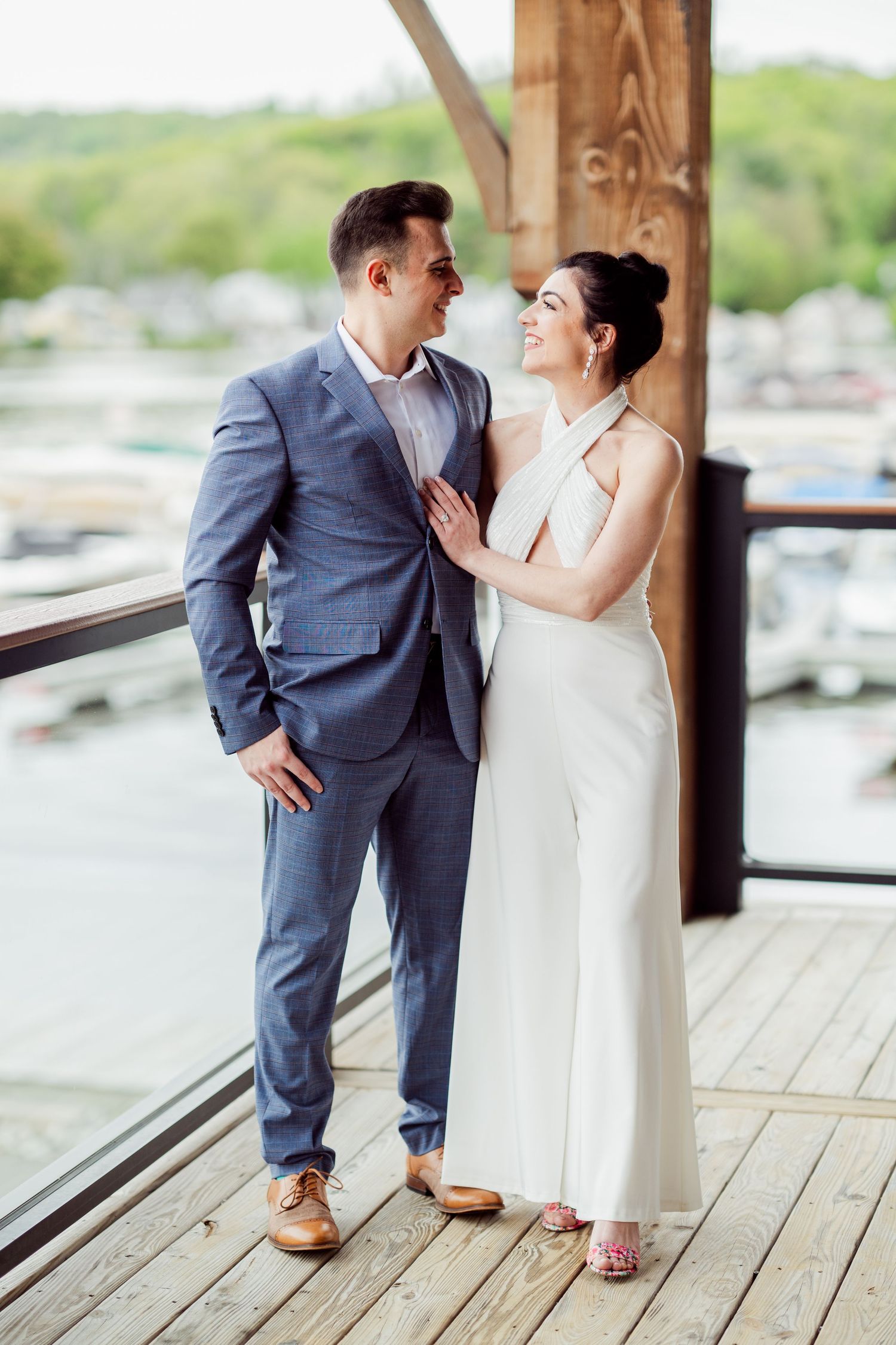 A couple shares intimate moments on a waterfront deck wearing formal wedding attire.
