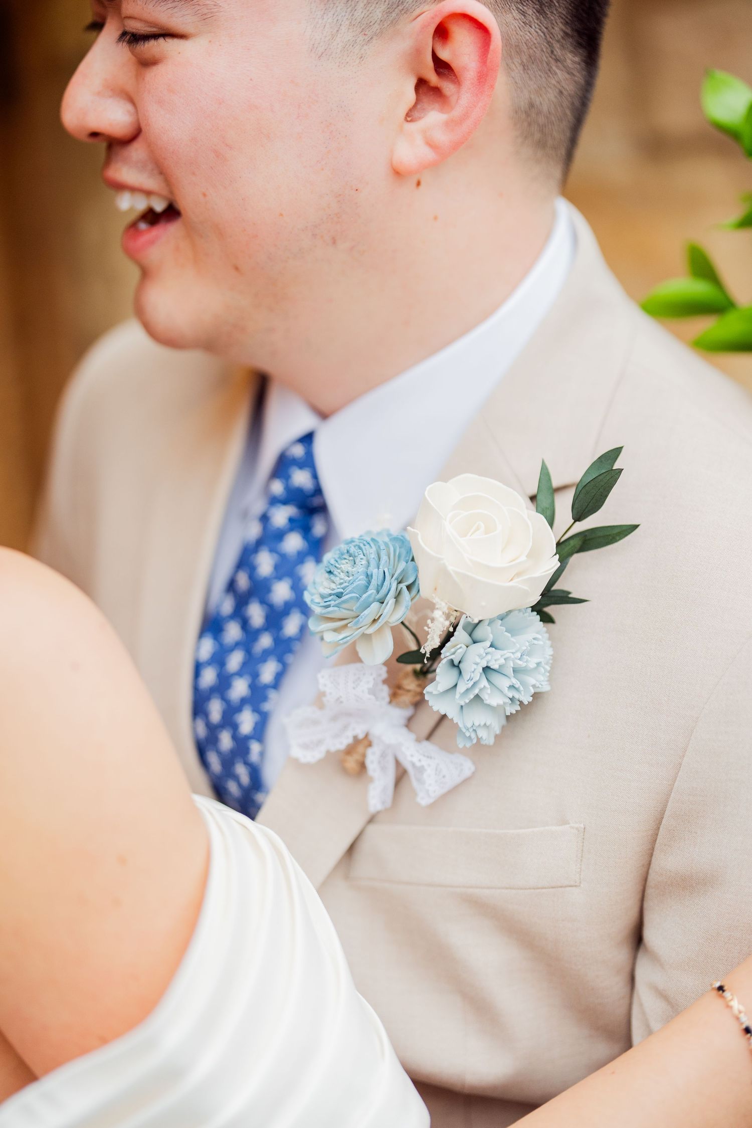 Close-up of groom's boutonniere featuring light blue and white flowers with a navy patterned tie.