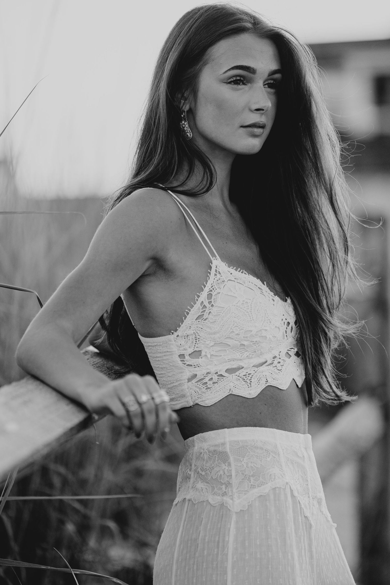 Black and white portrait of woman in white lace bralette and skirt posing outdoors at dusk.