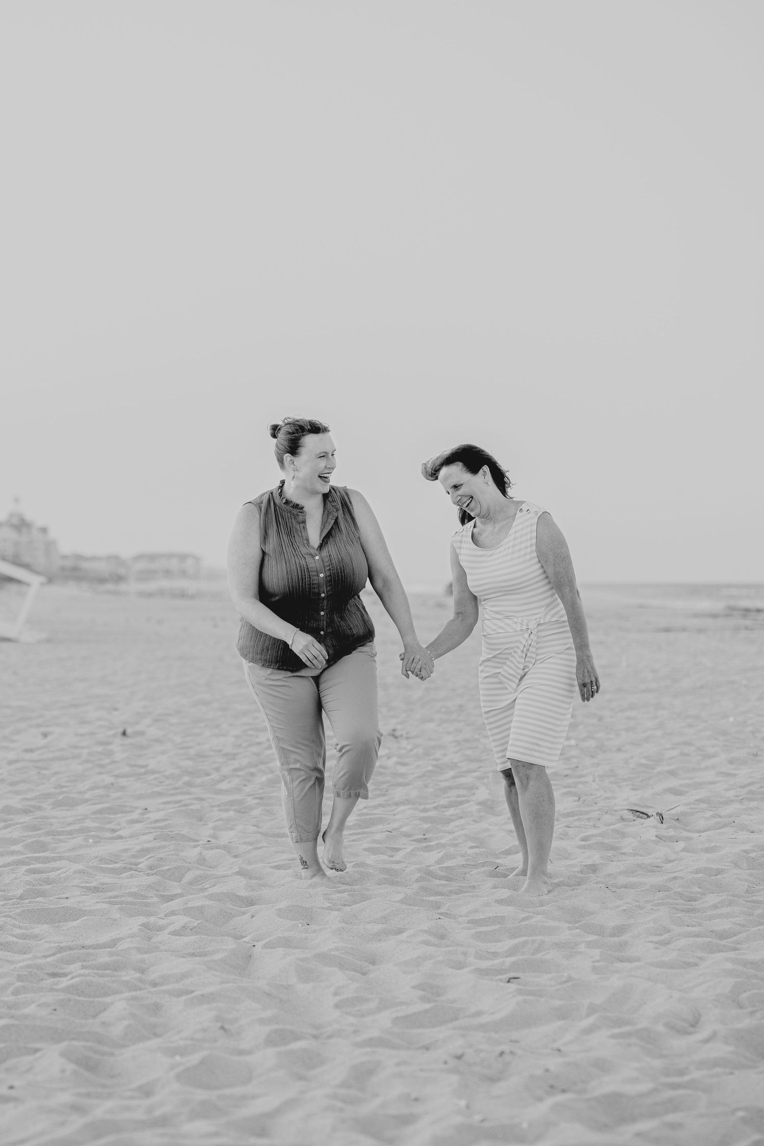 Two women holding hands and walking on a sandy beach in black and white photography.