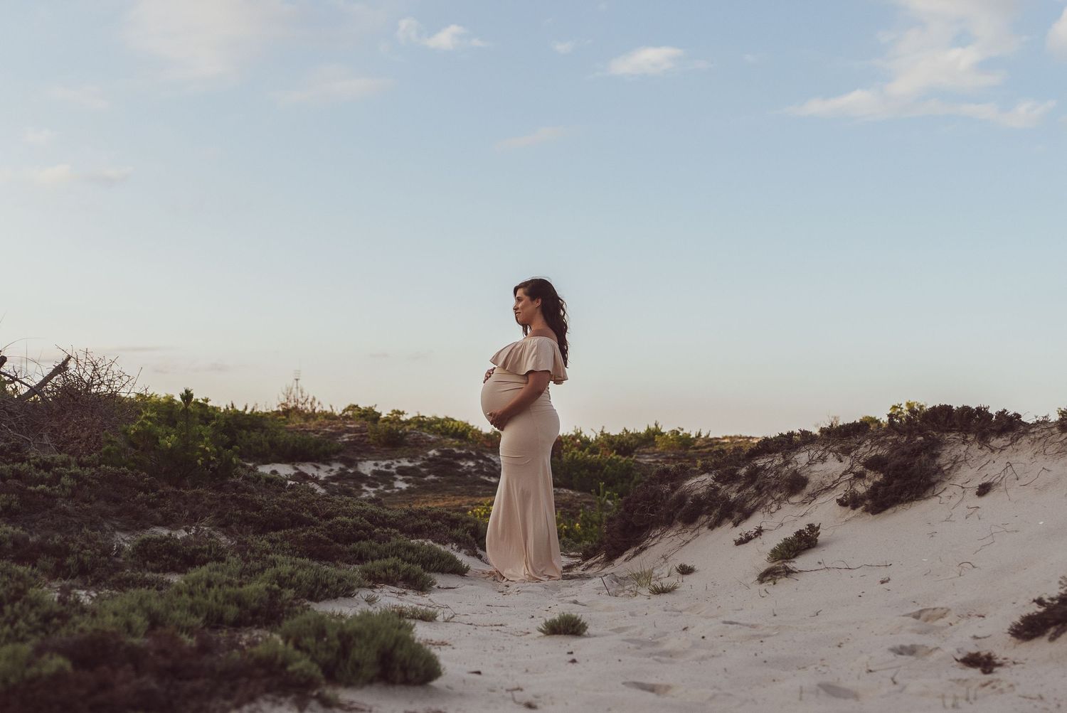 Woman in white dress standing alone on sandy dunes at sunset.
