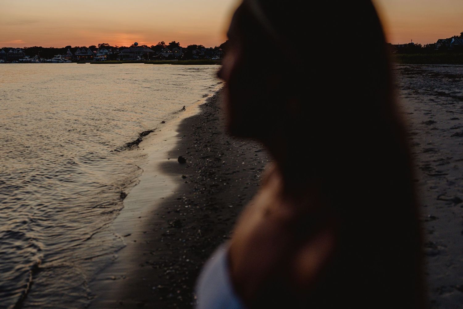 Woman with long dark hair sitting on a sandy beach during a golden sunset.