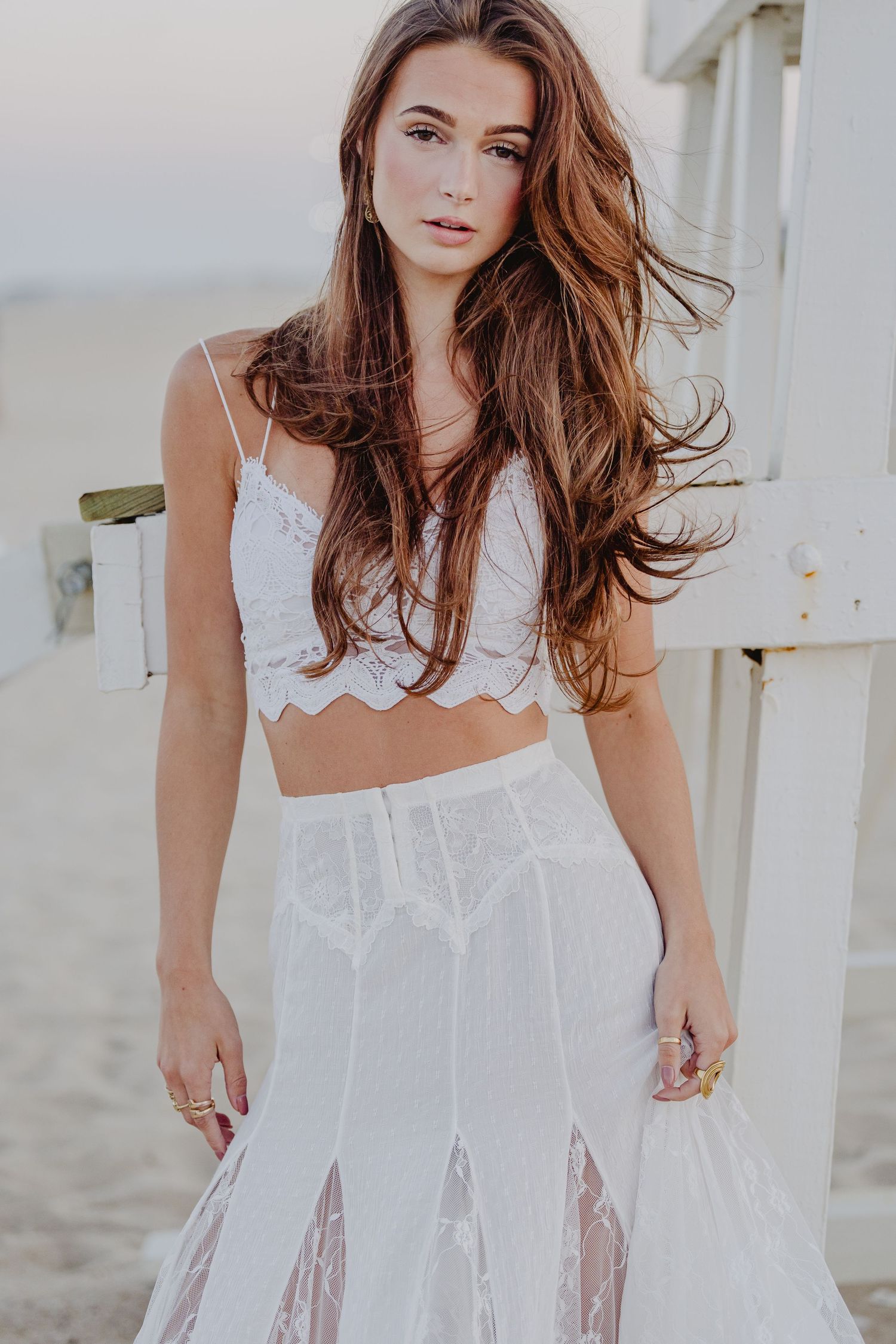 Young woman in white lace crop top and sheer maxi skirt posing on a beach at sunset. Lifeguard stand in Sea Girt, new Jersey