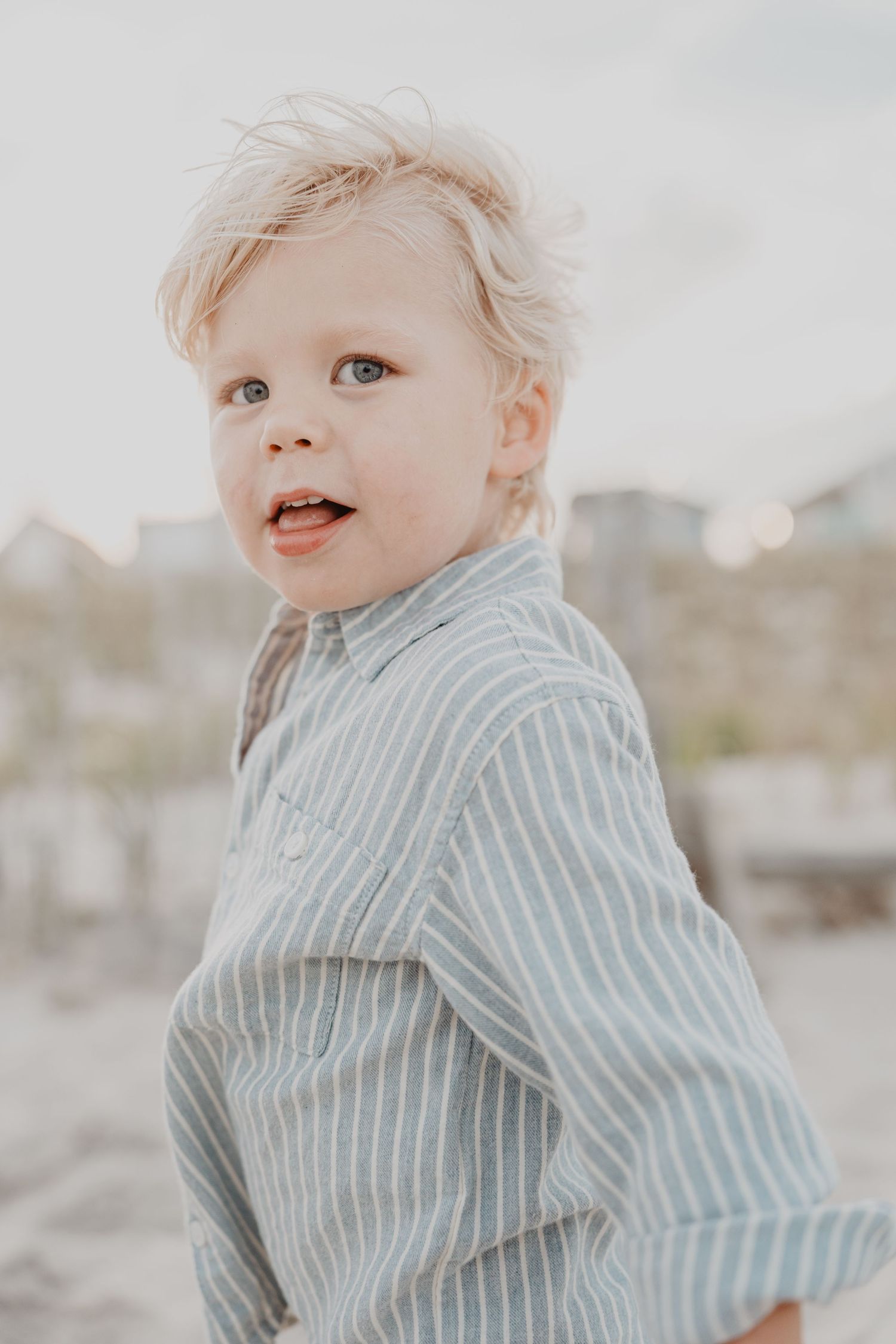 Close-up portrait of toddler wearing blue striped shirt on beach.
