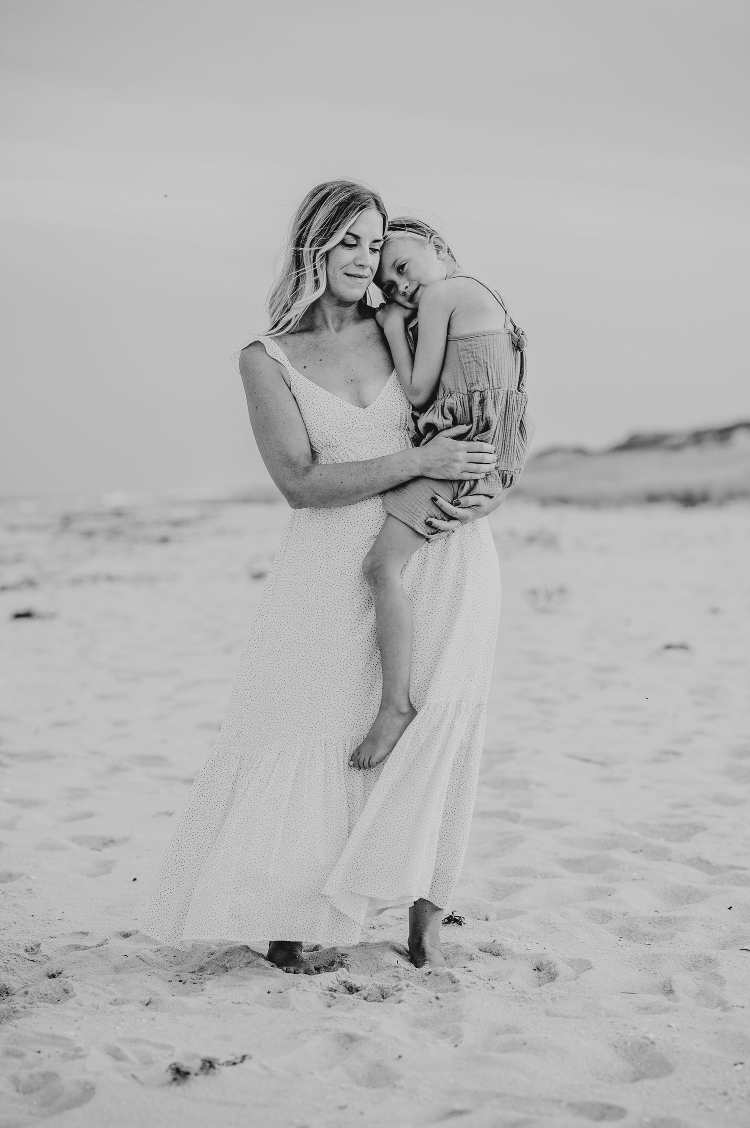 Black and white beach portrait of mother and child embracing on sand.