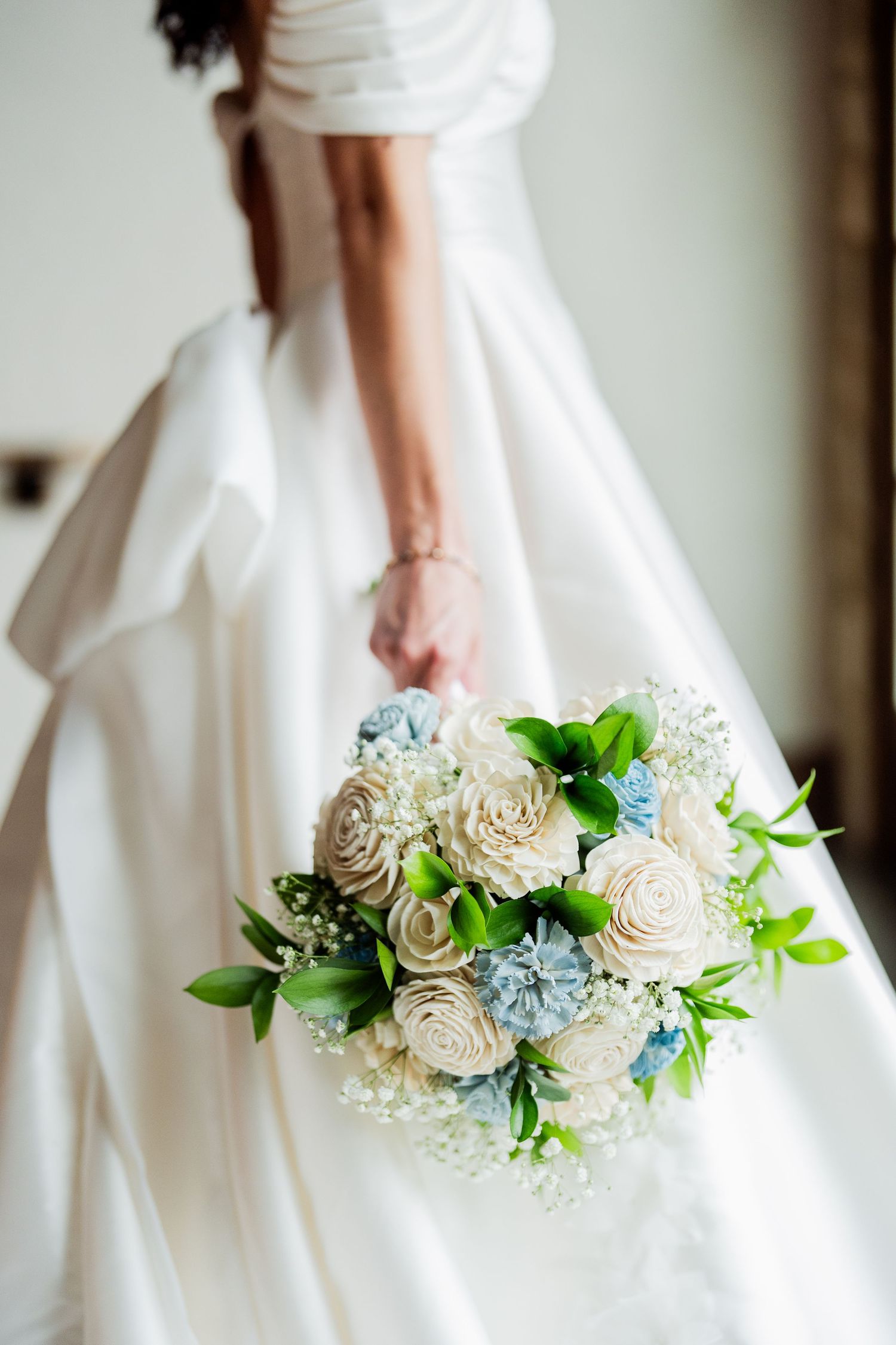 Close-up view of a delicate white and blue wedding bouquet held against a flowing white wedding dress.