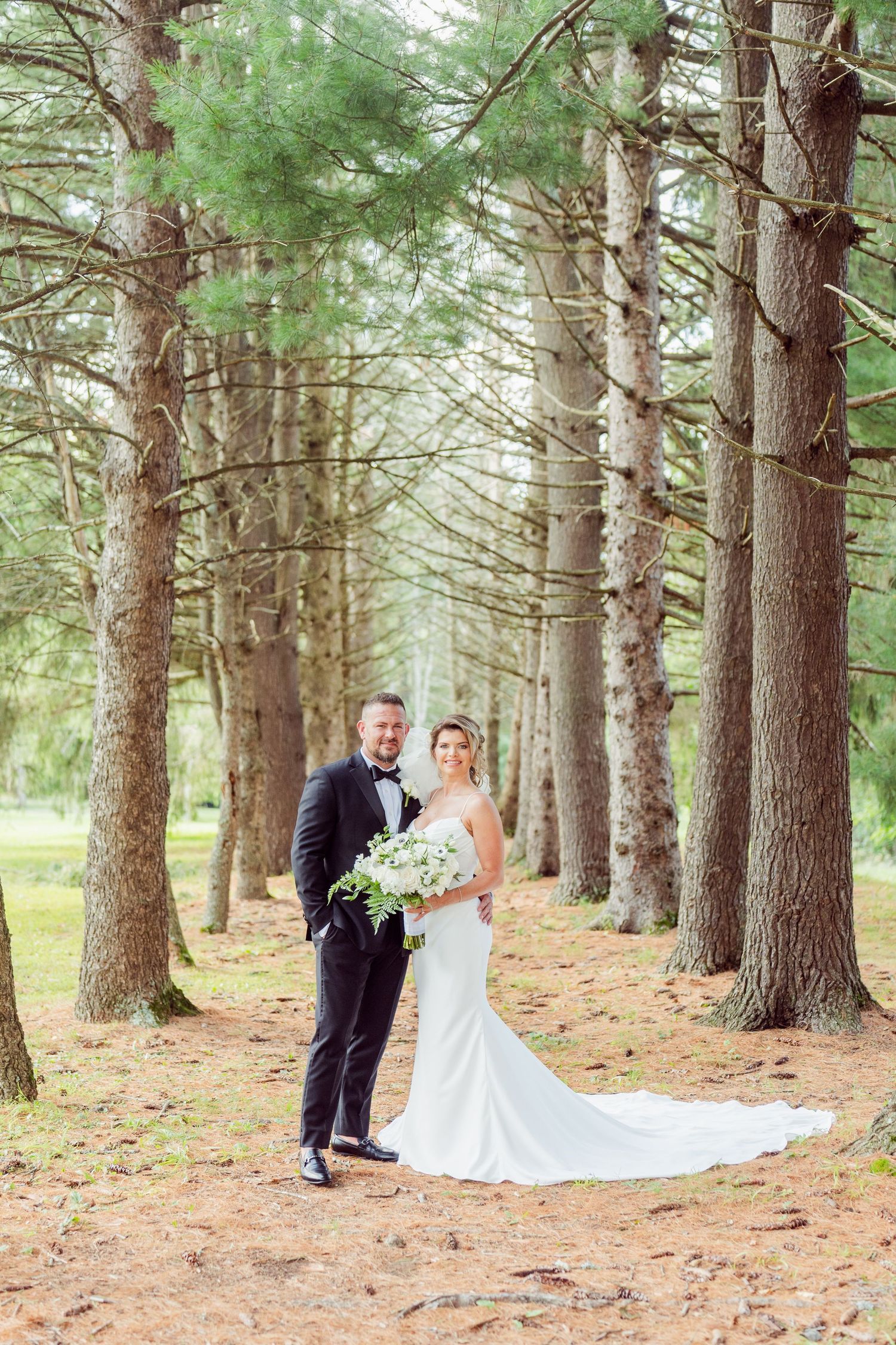 Wedding photography session in a majestic pine tree forest with needles covering the ground.