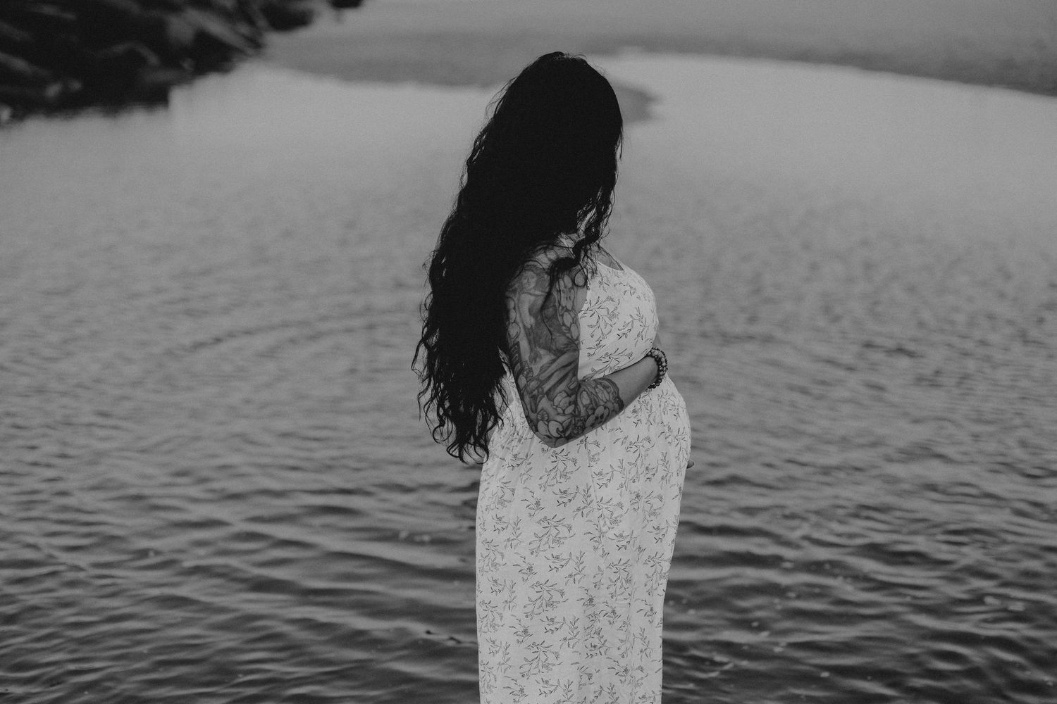 Silhouette of a woman in a flowing dress standing by the water at dusk.
