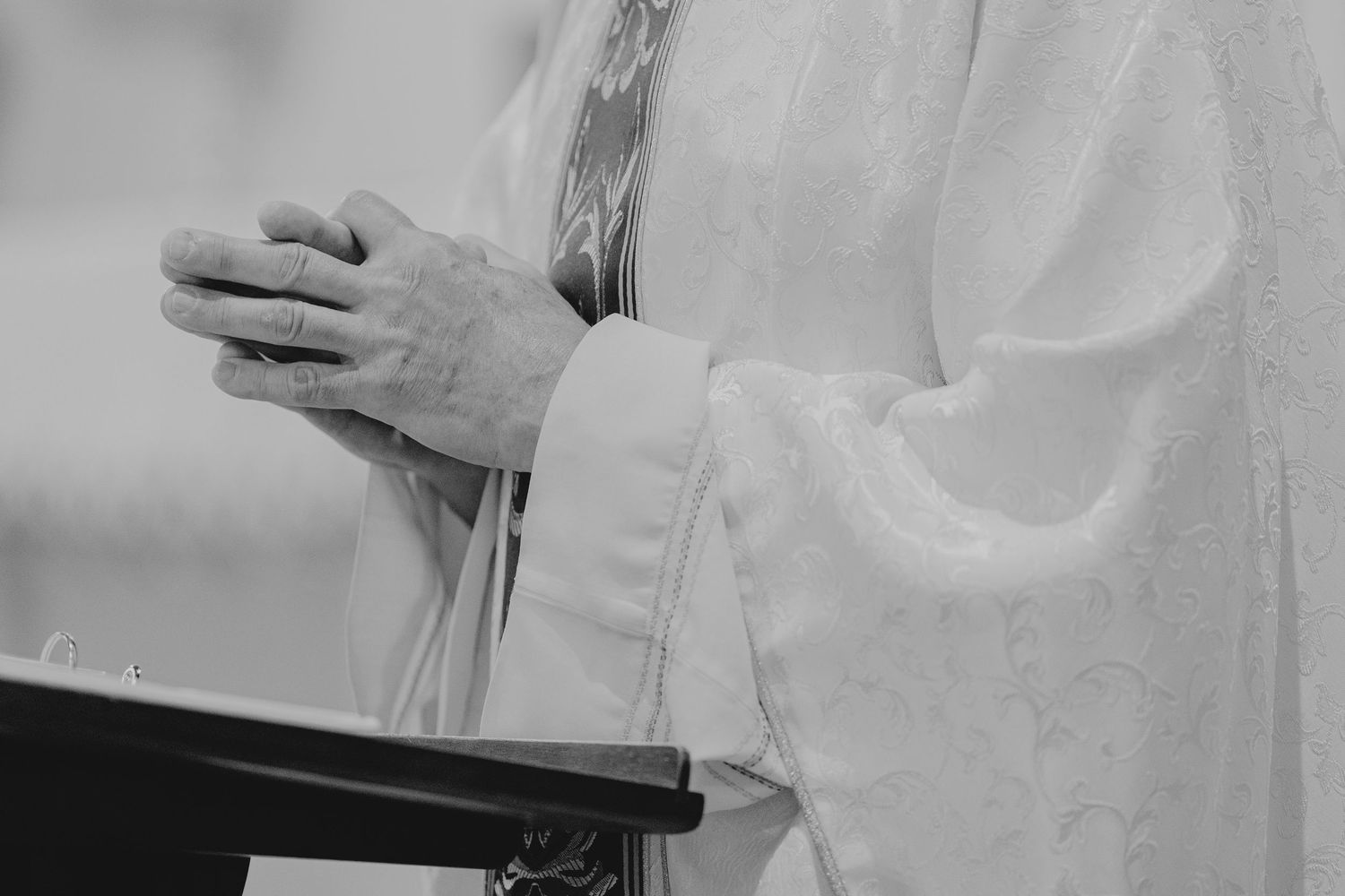 Close-up of a priest in white vestments clasping hands at a church altar during a religious ceremony.