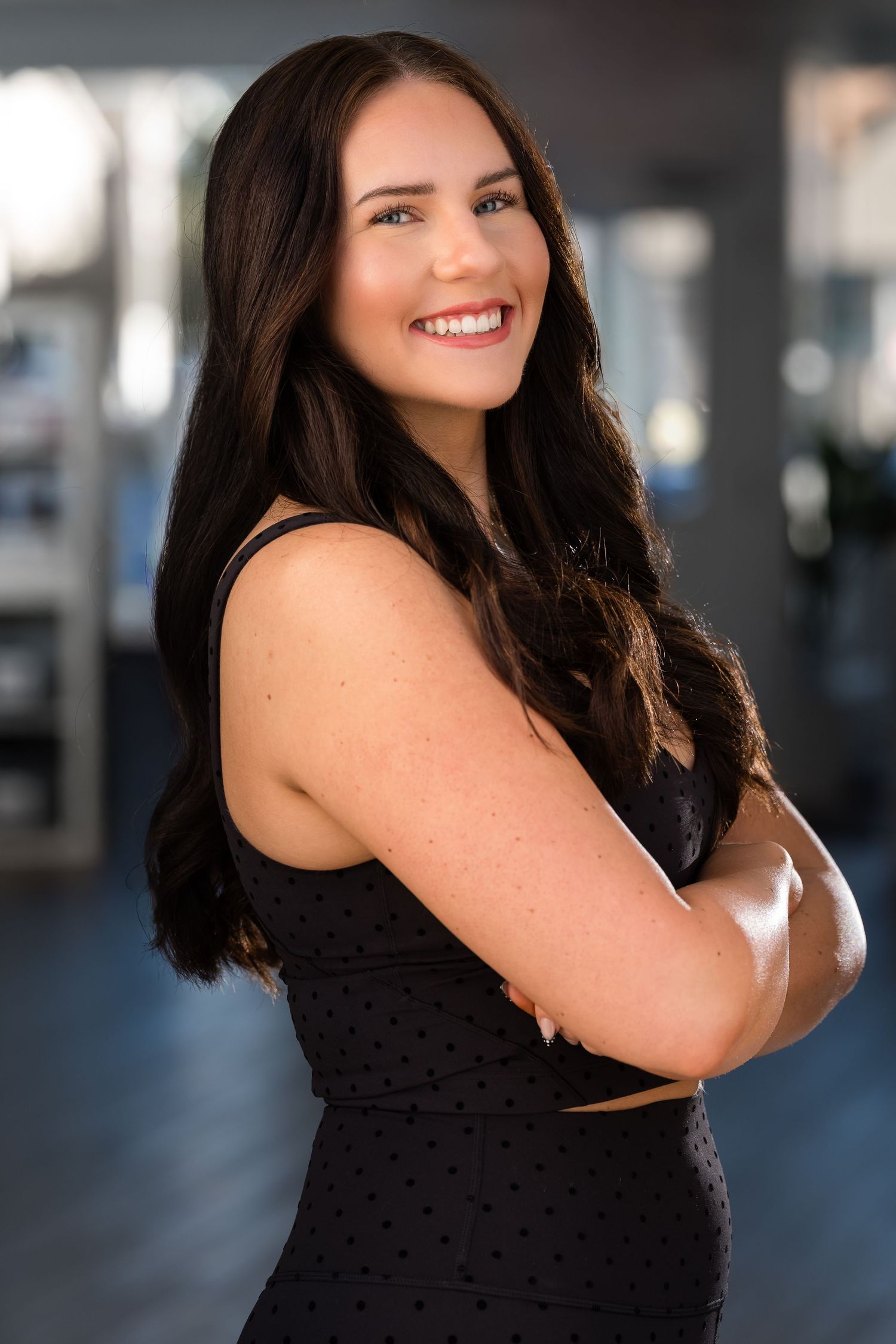 Woman in black sleeveless top poses against blurred background with bright smile.