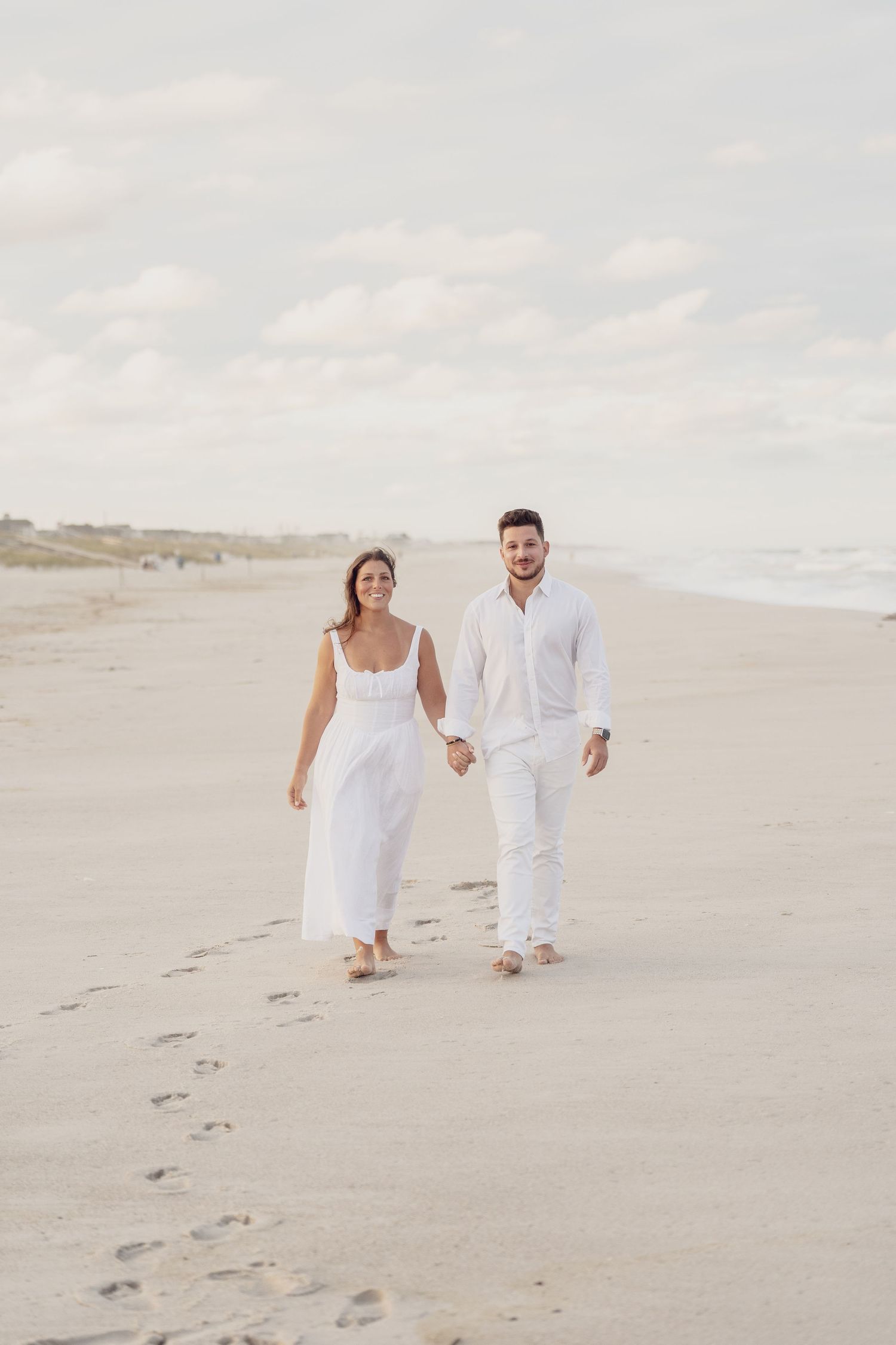 Footprints trail behind a couple as they walk hand in hand along a peaceful beach.