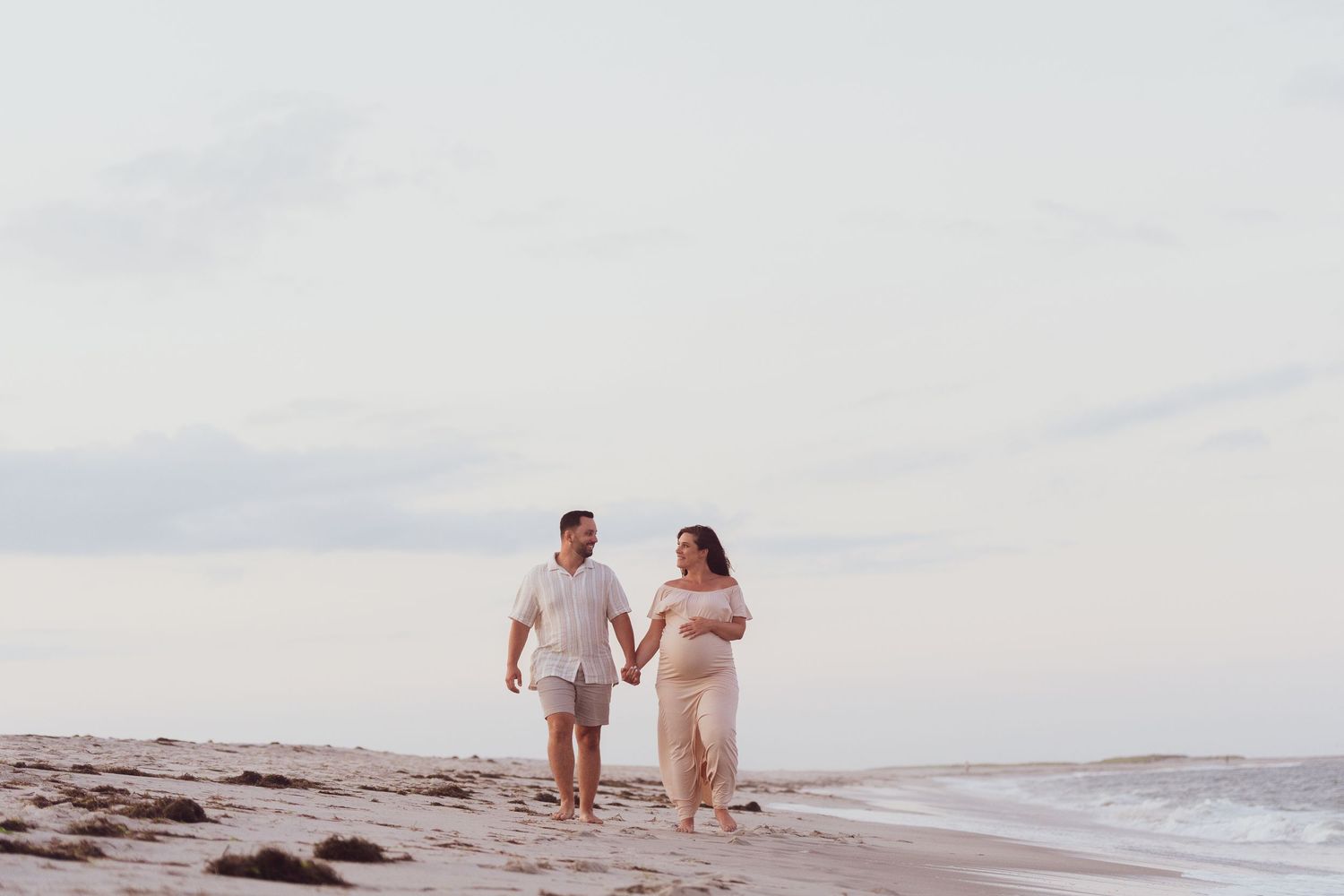 Couple walking hand in hand along peaceful beach shoreline.