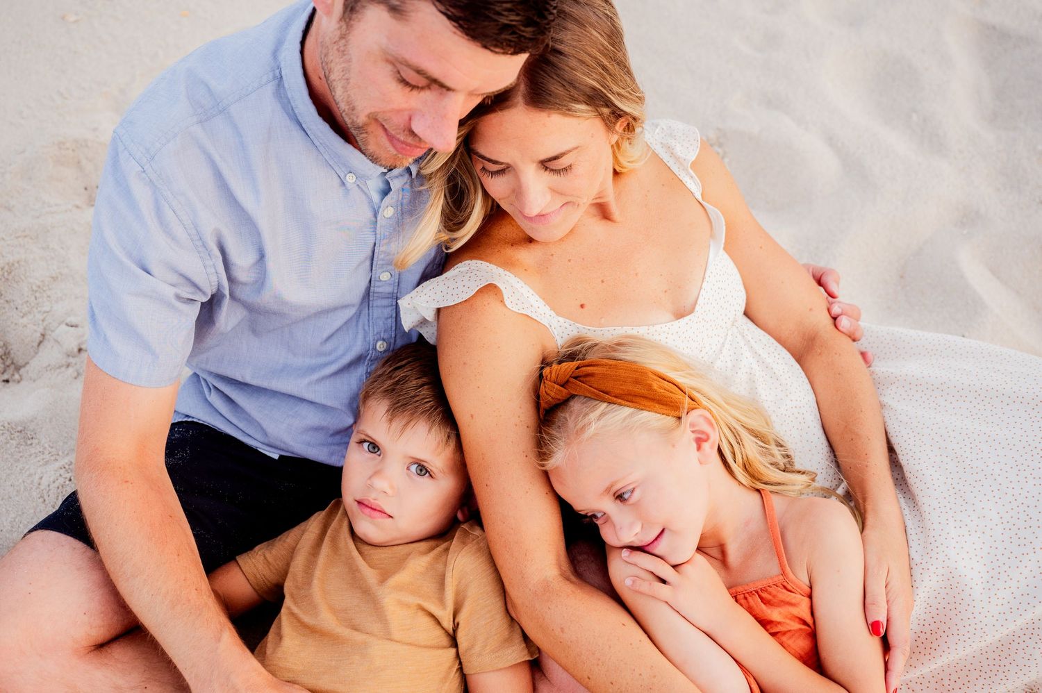 Family lying together on white bedding while sharing tender moments of connection and affection.