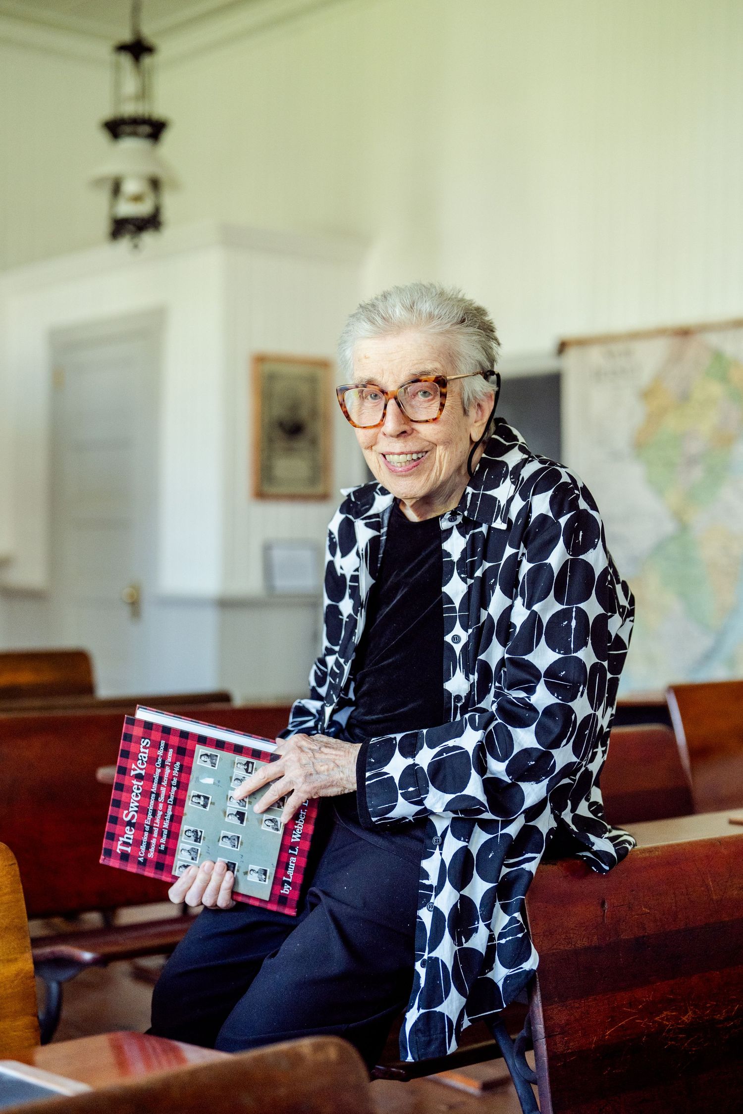 A person in a black and white polka dot jacket sits in a church pew holding a red book.