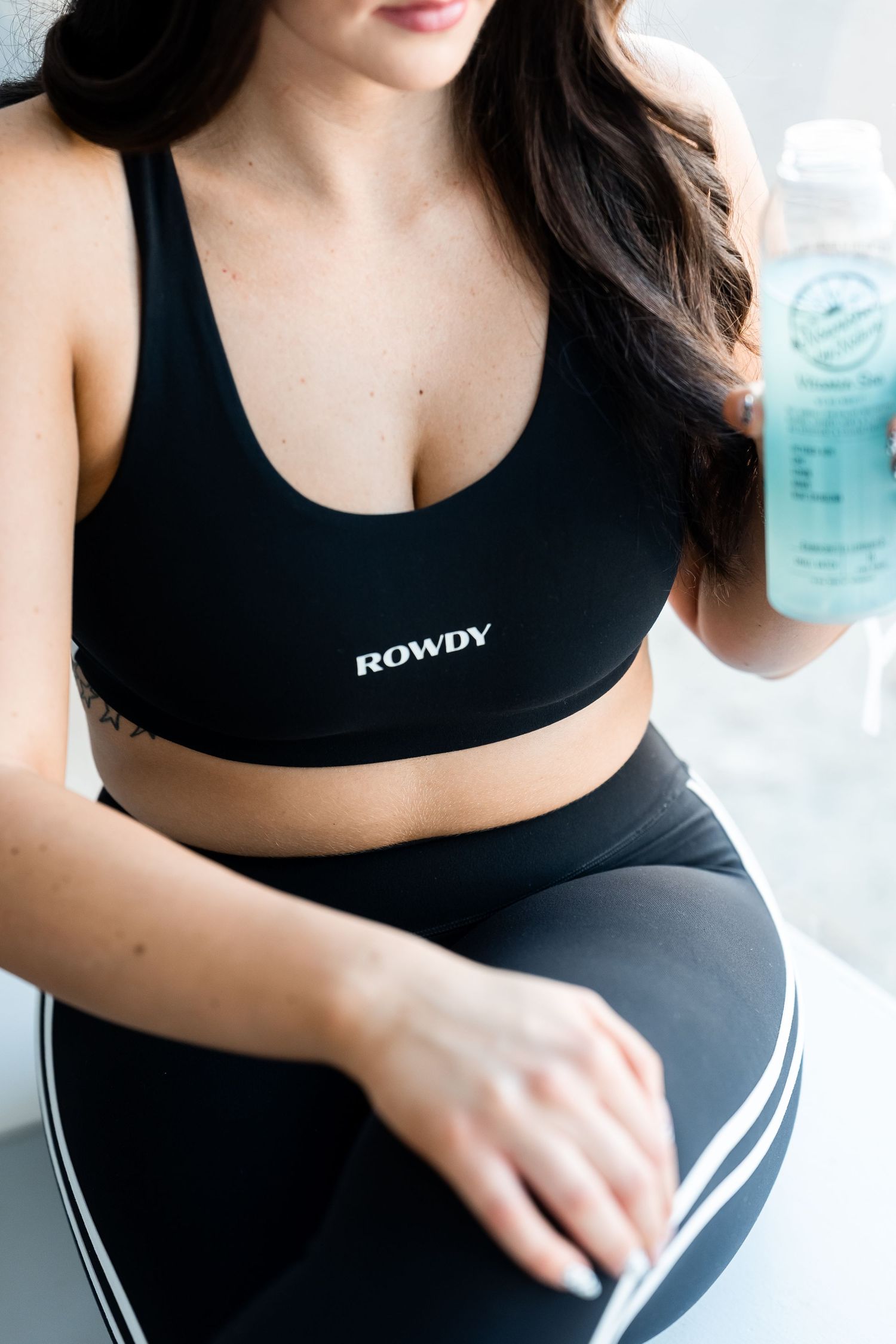 Athletic woman in black sports bra and leggings with striped details holds a water bottle during workout.