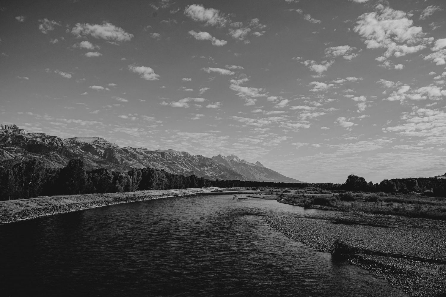 Dramatic black and white panoramic landscape with mountains and clouds stretching across a rugged terrain.