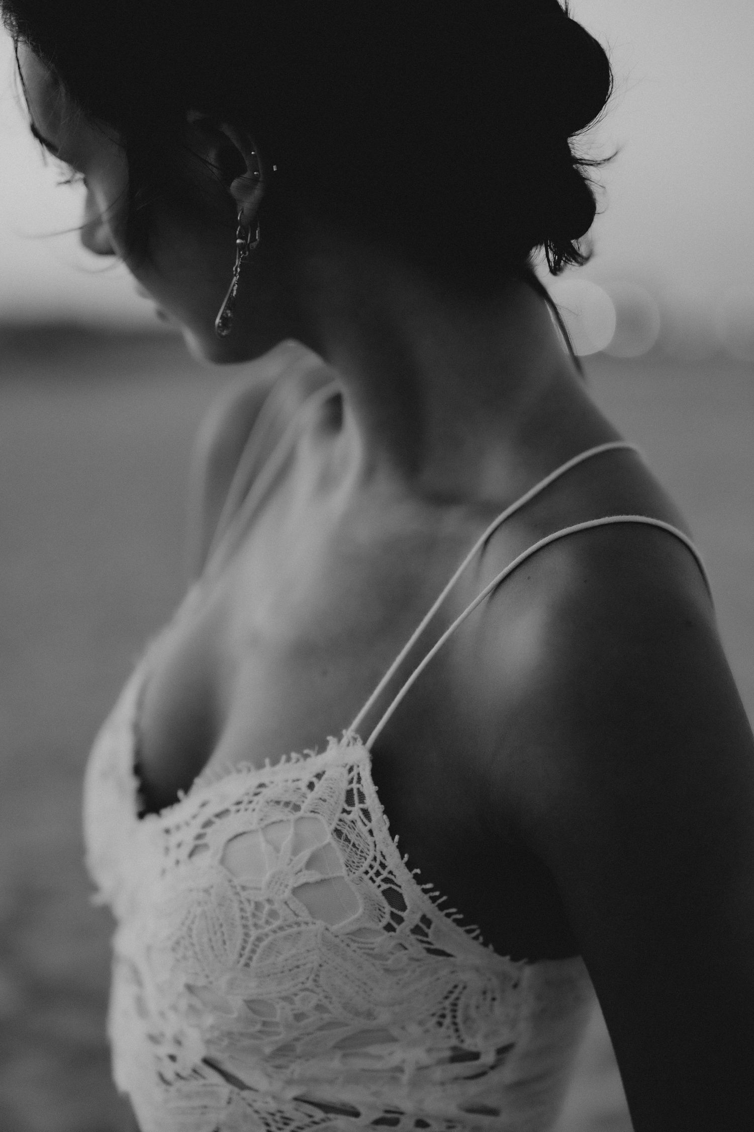 Black and white close-up of a woman wearing a white lace camisole and silver hoop earring.