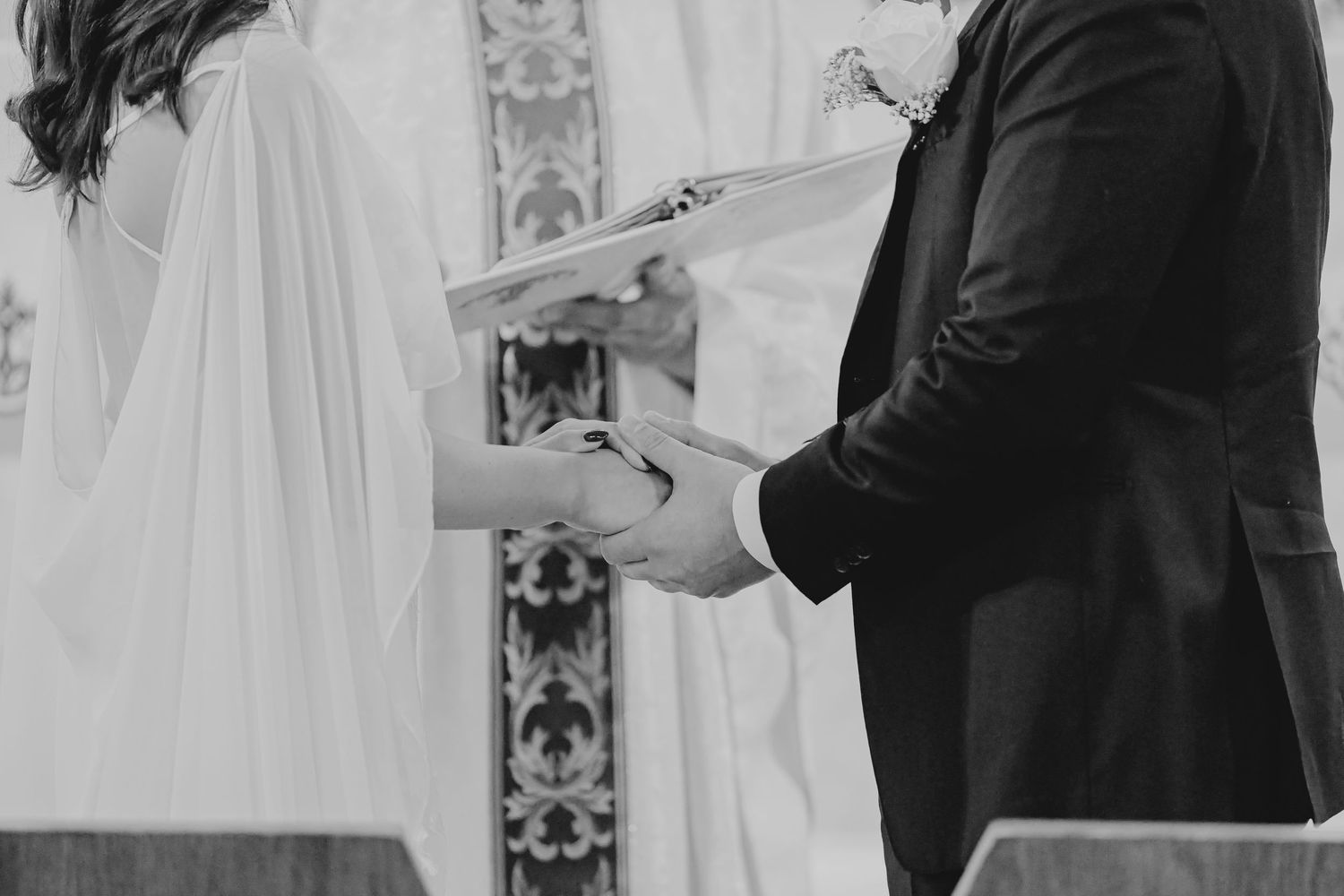 Black and white photo of bride and groom exchanging vows and holding hands at a church wedding ceremony.