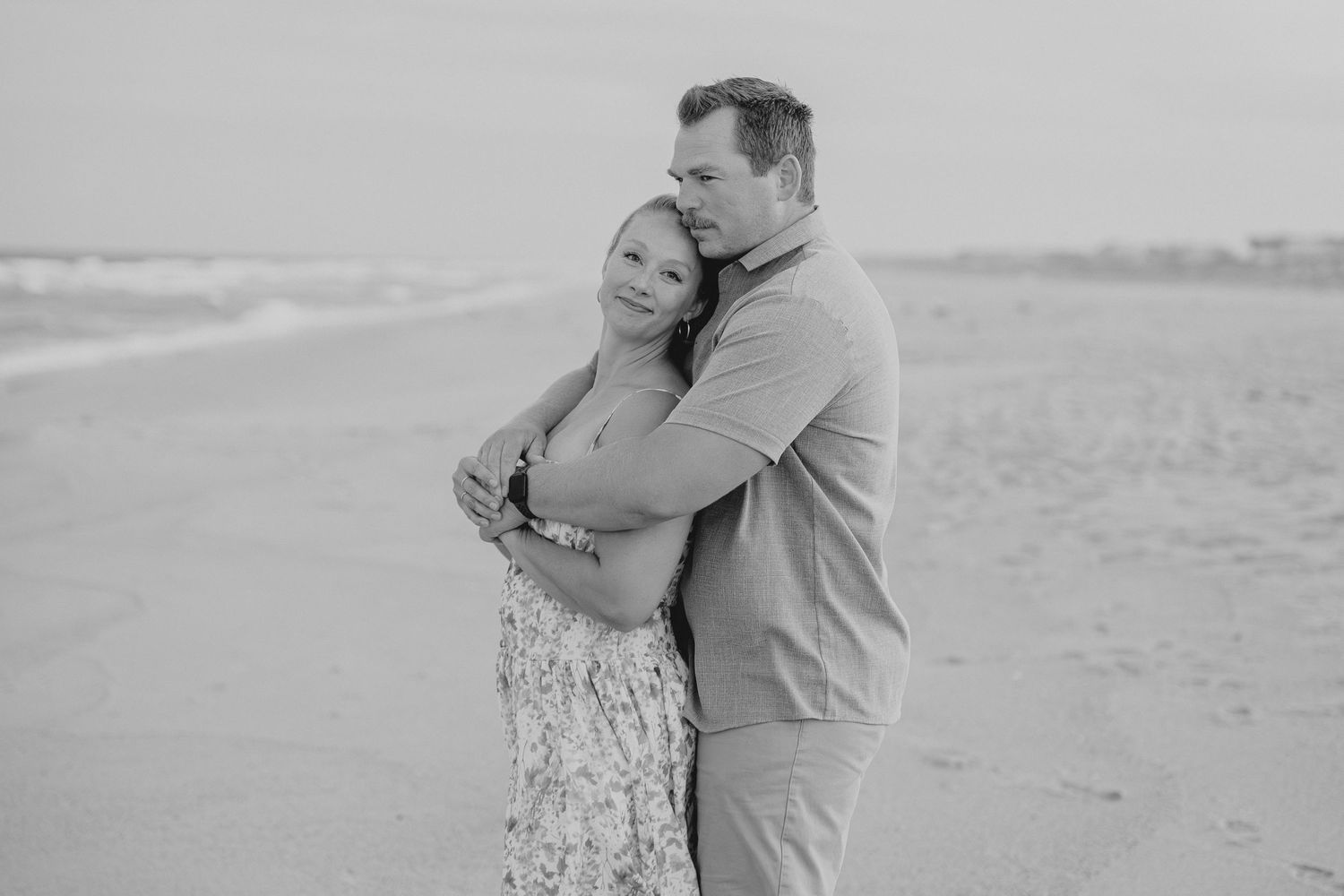 Romantic beach engagement photos showing a couple embracing on the sand.