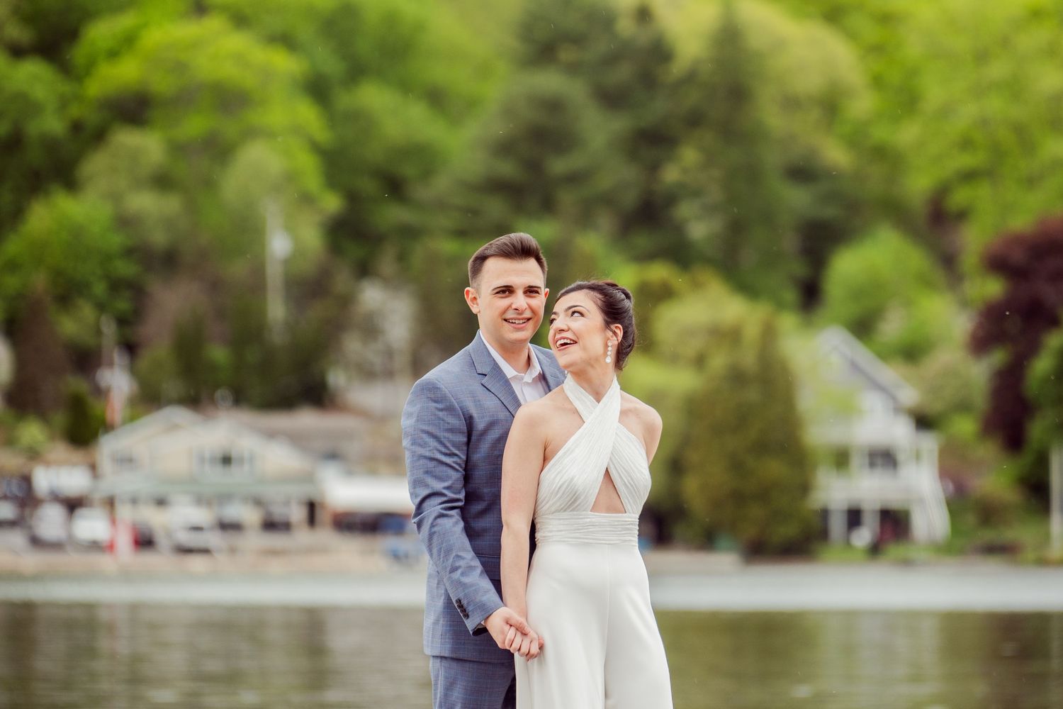Couple poses for romantic waterfront photos with lush greenery in background.