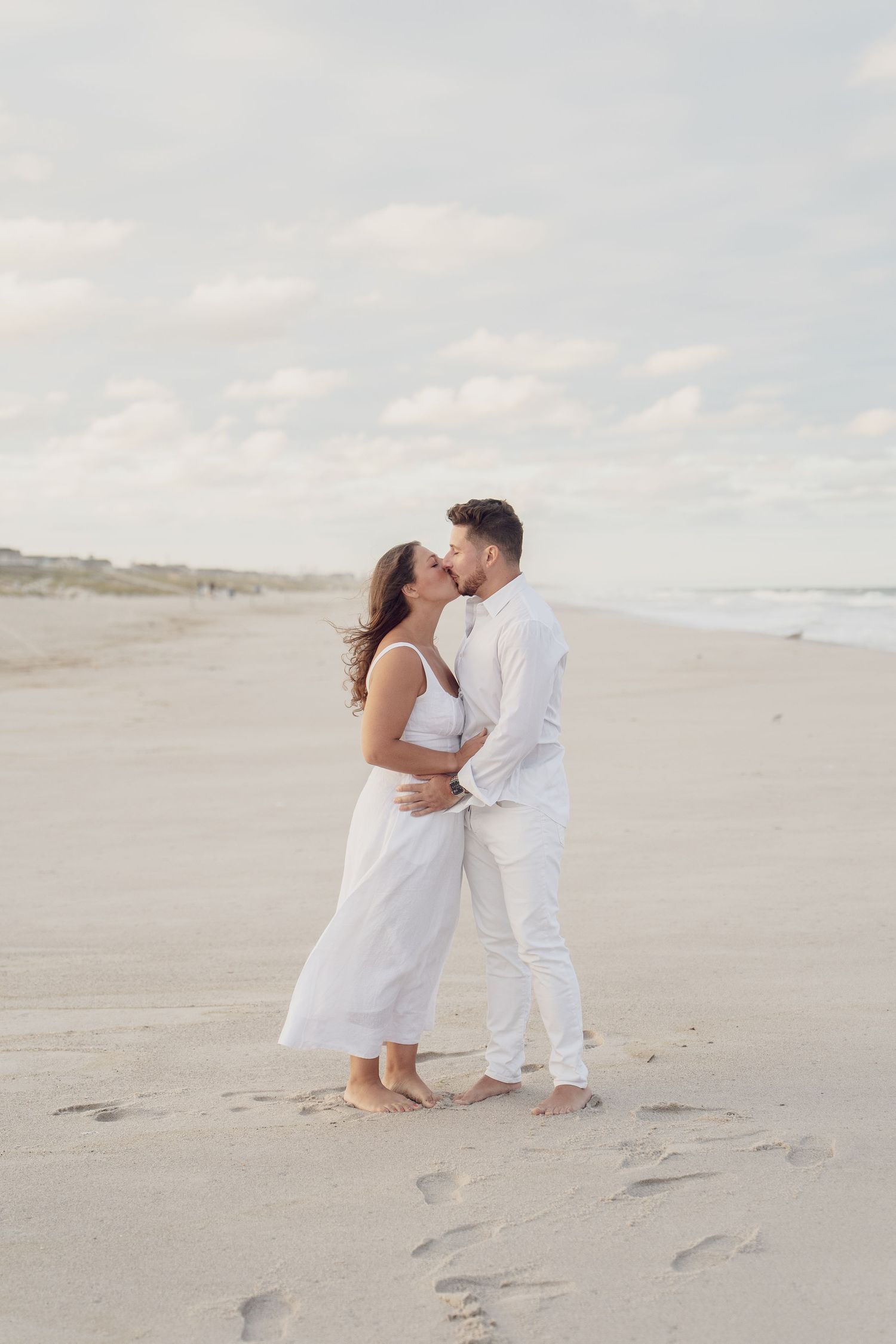 Intimate beach portraits of couple in white clothing sharing romantic moments on sandy shore.
