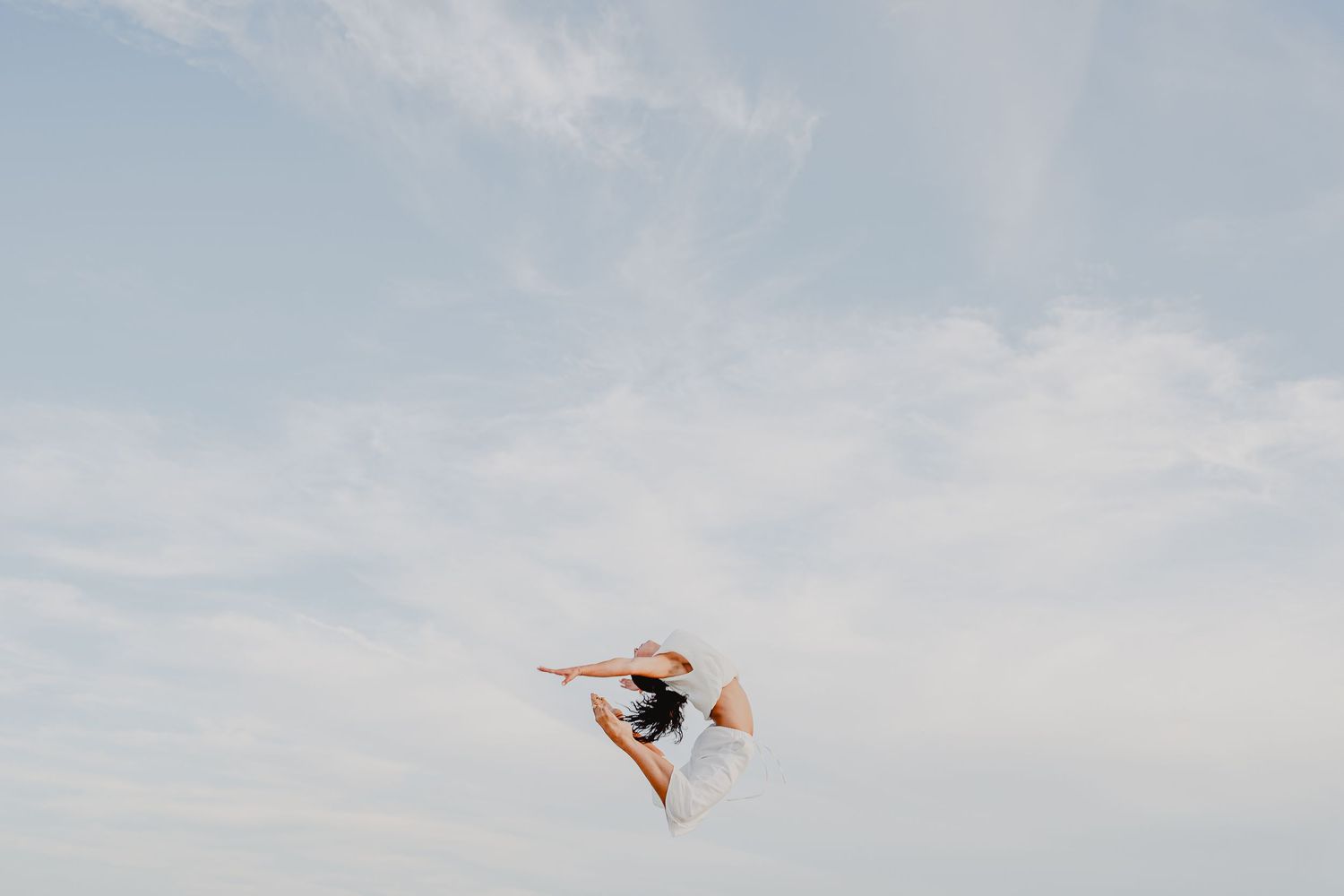 A dancer leaps gracefully against a soft blue sky, captured mid-air in an elegant pose.