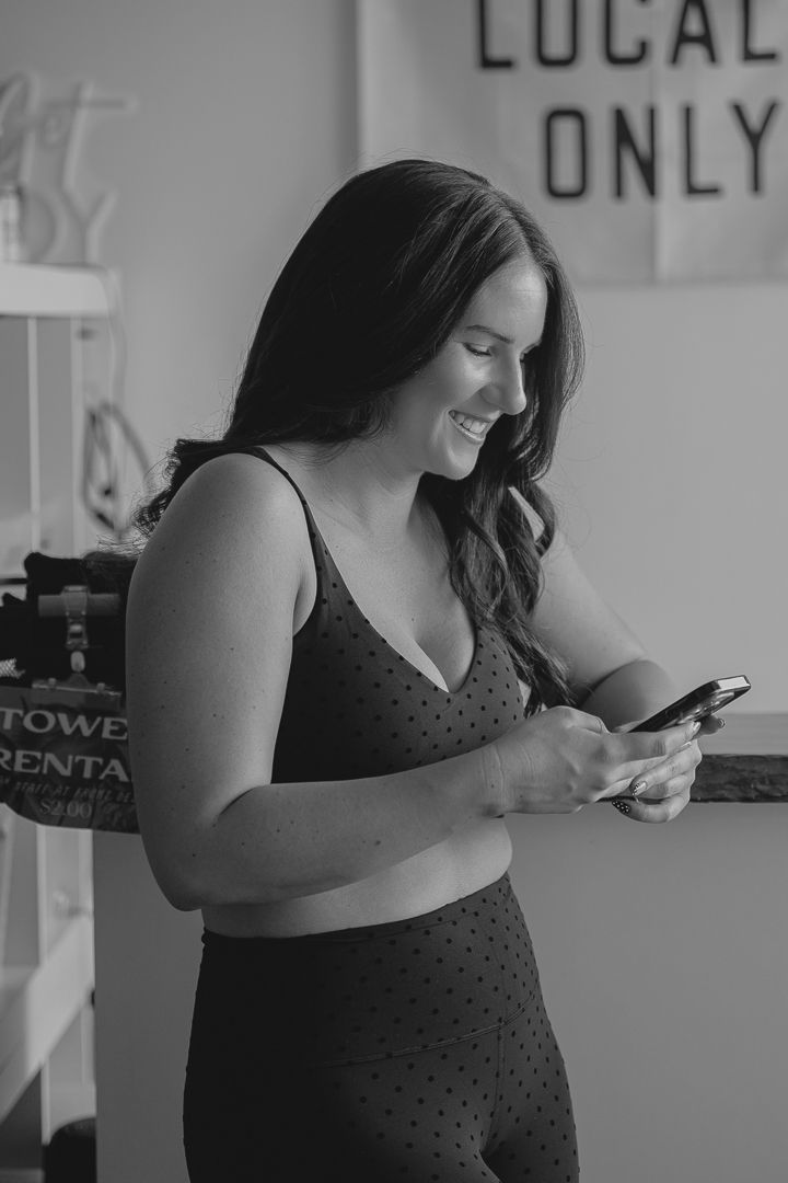 A person in a dark sleeveless top looking down at their mobile phone in a black and white photograph.