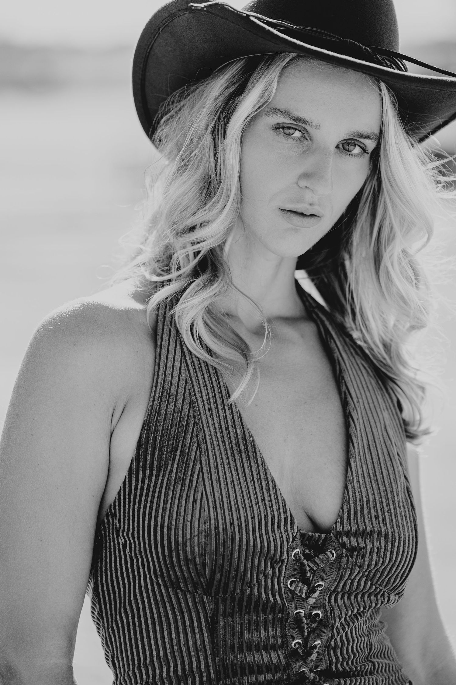 Black and white portrait of a blonde woman wearing a wide-brim cowboy hat and lace-up halter top.